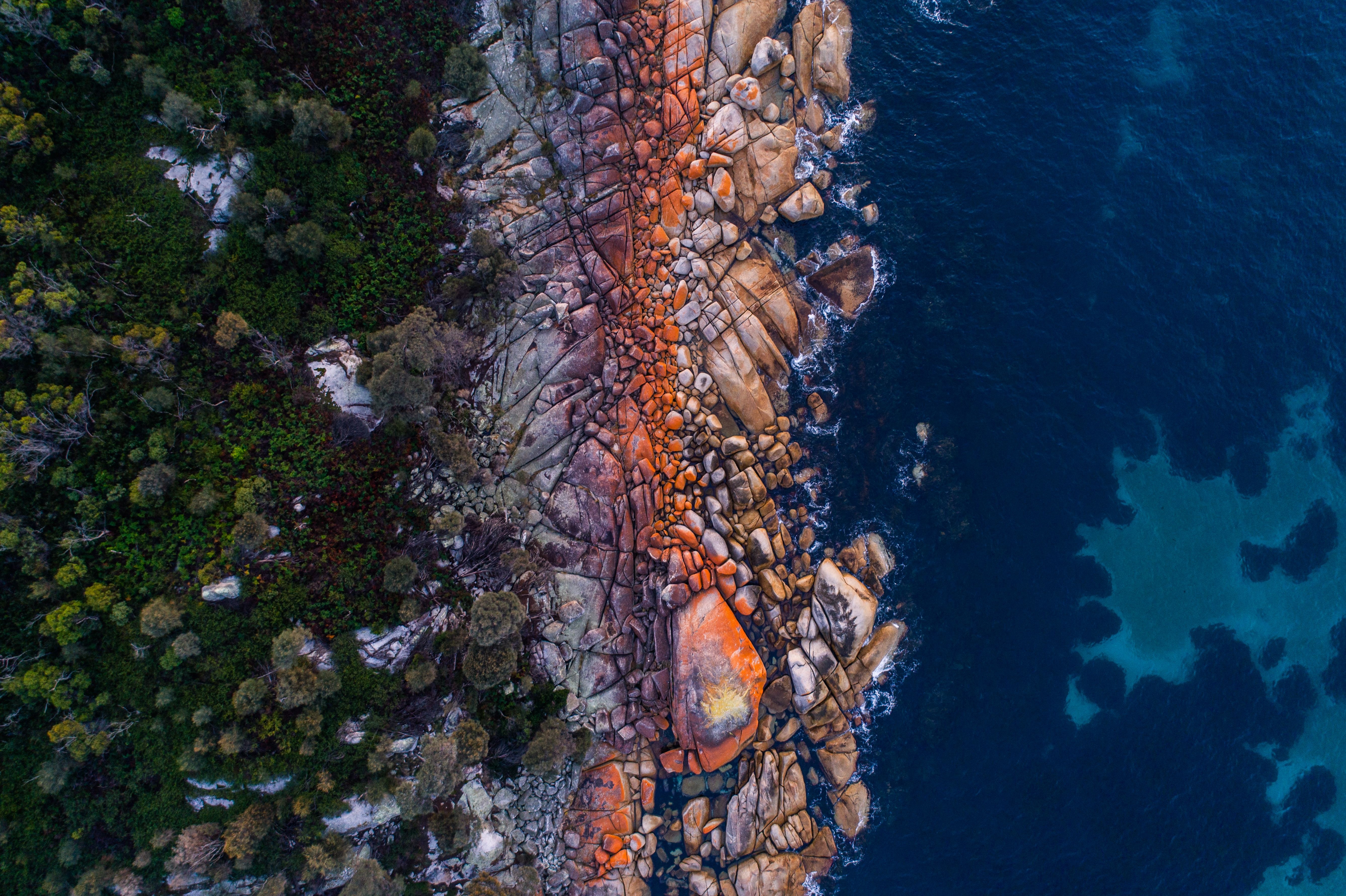 Aerial view of orange lichen covered granite boulders meeting deep blue ocean at larapuna / Bay of Fires area