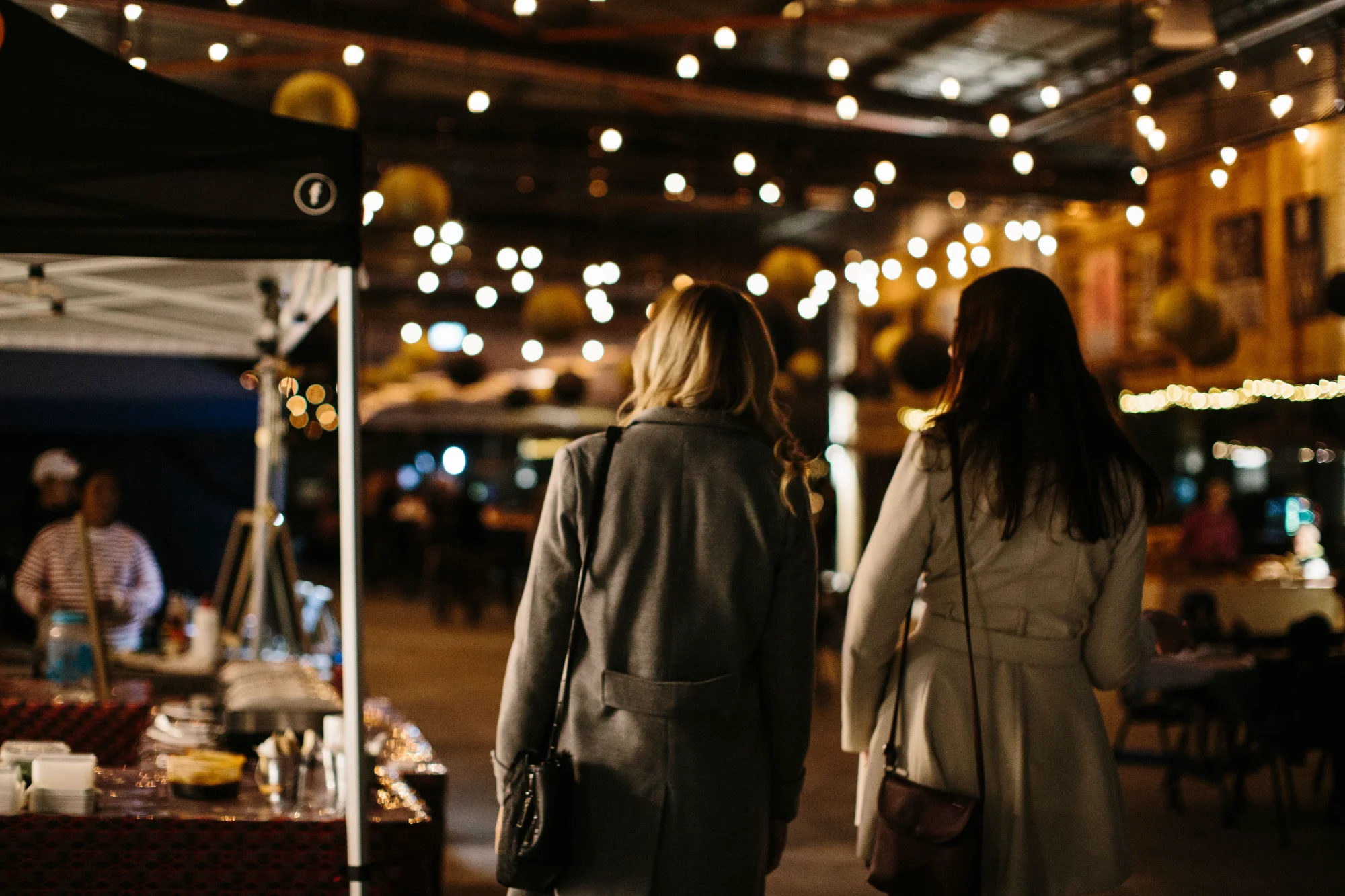 Two visitors strolling beneath string lights at the Providore Market night, Devonport