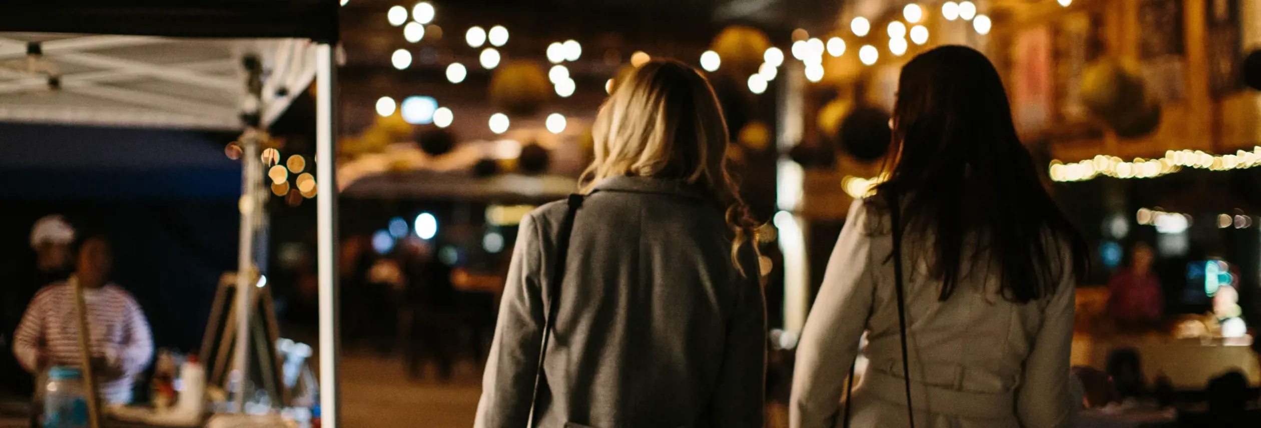 Two visitors strolling beneath string lights at the Providore Market night, Devonport