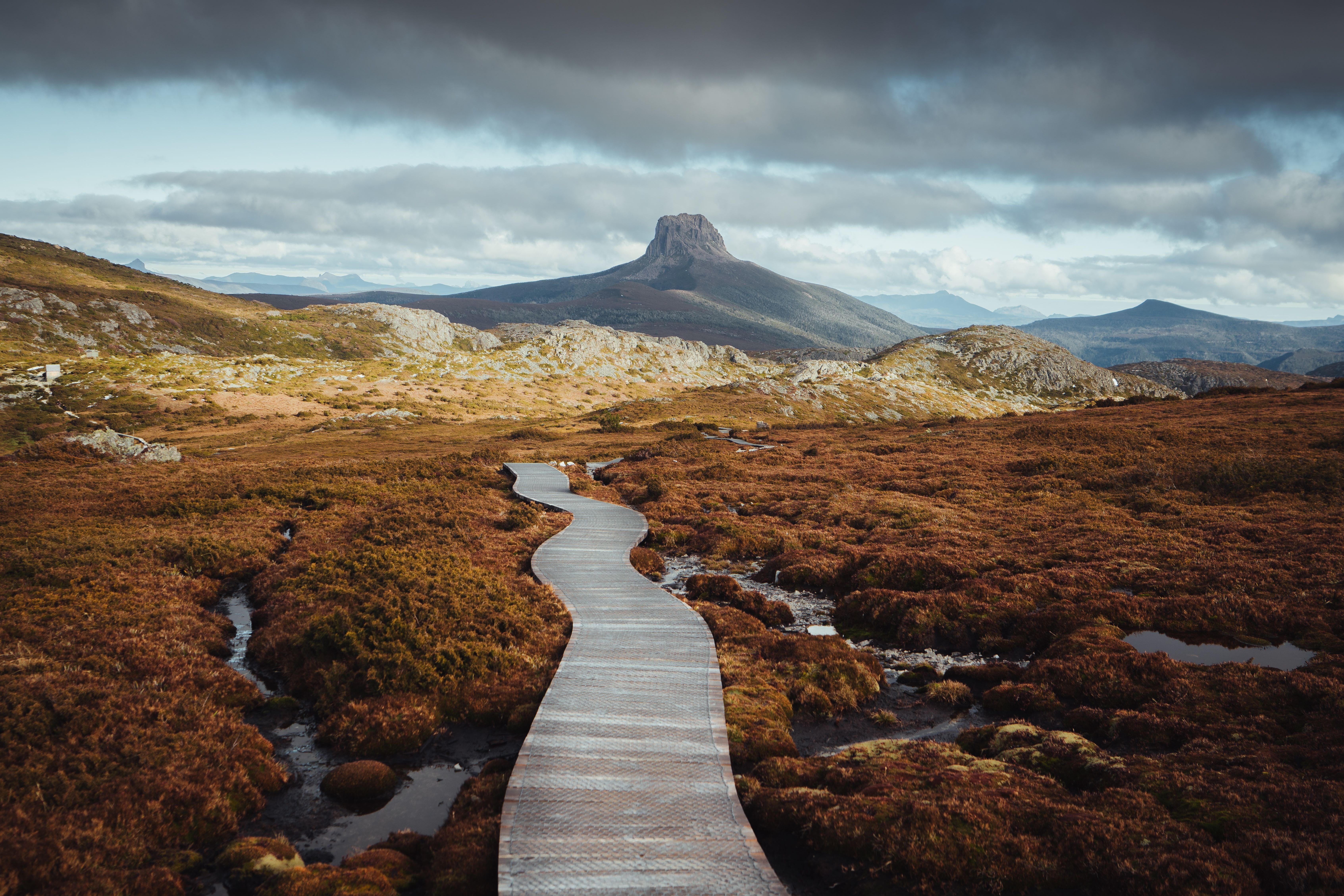 A boardwalk winds through alpine moorland toward a distinctive rocky peak on the Overland Track, Cradle Mountain