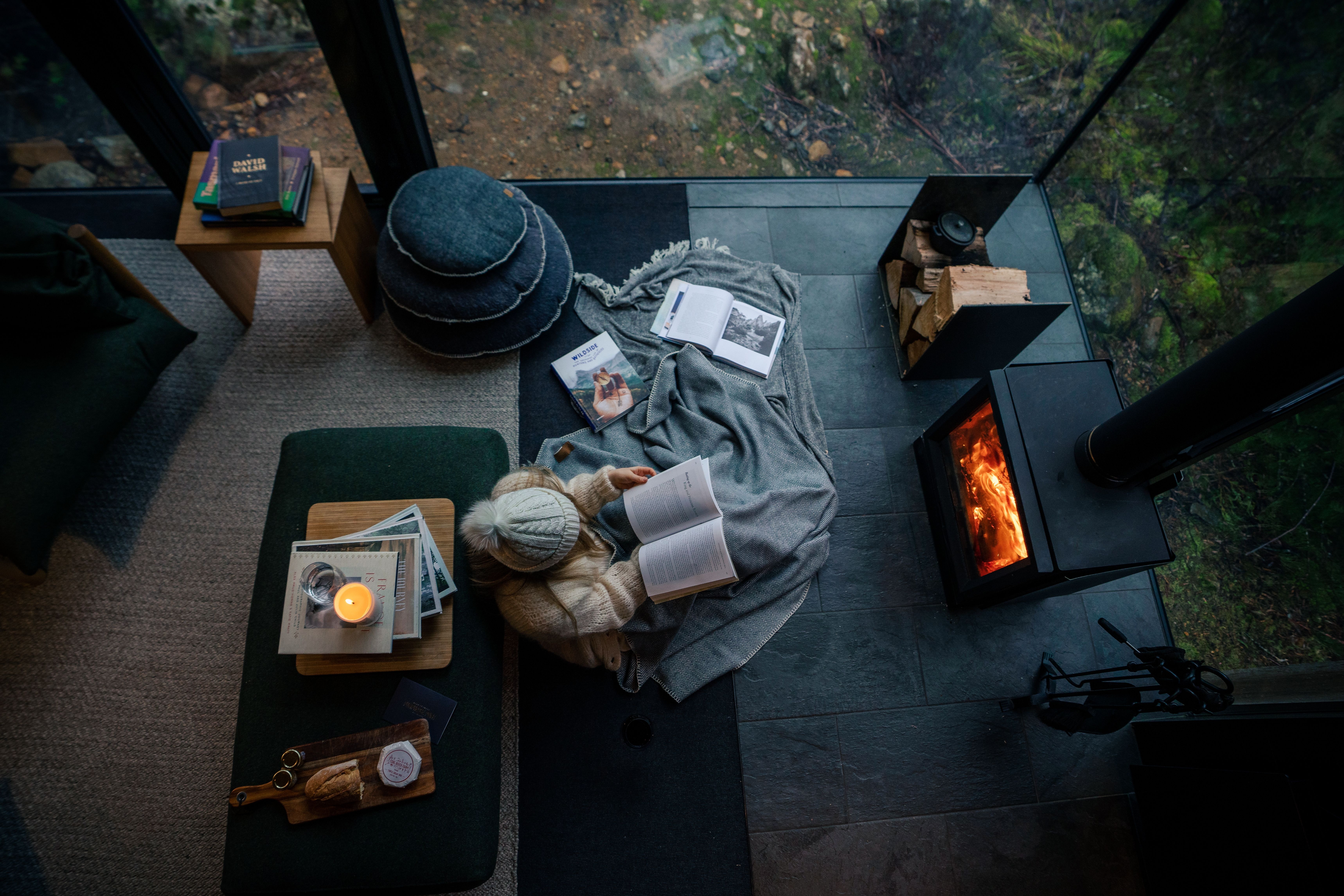 Overhead view of a person reading by a fireplace wrapped in a blanket with books and a candle at Pumphouse Point, Lake St Clair