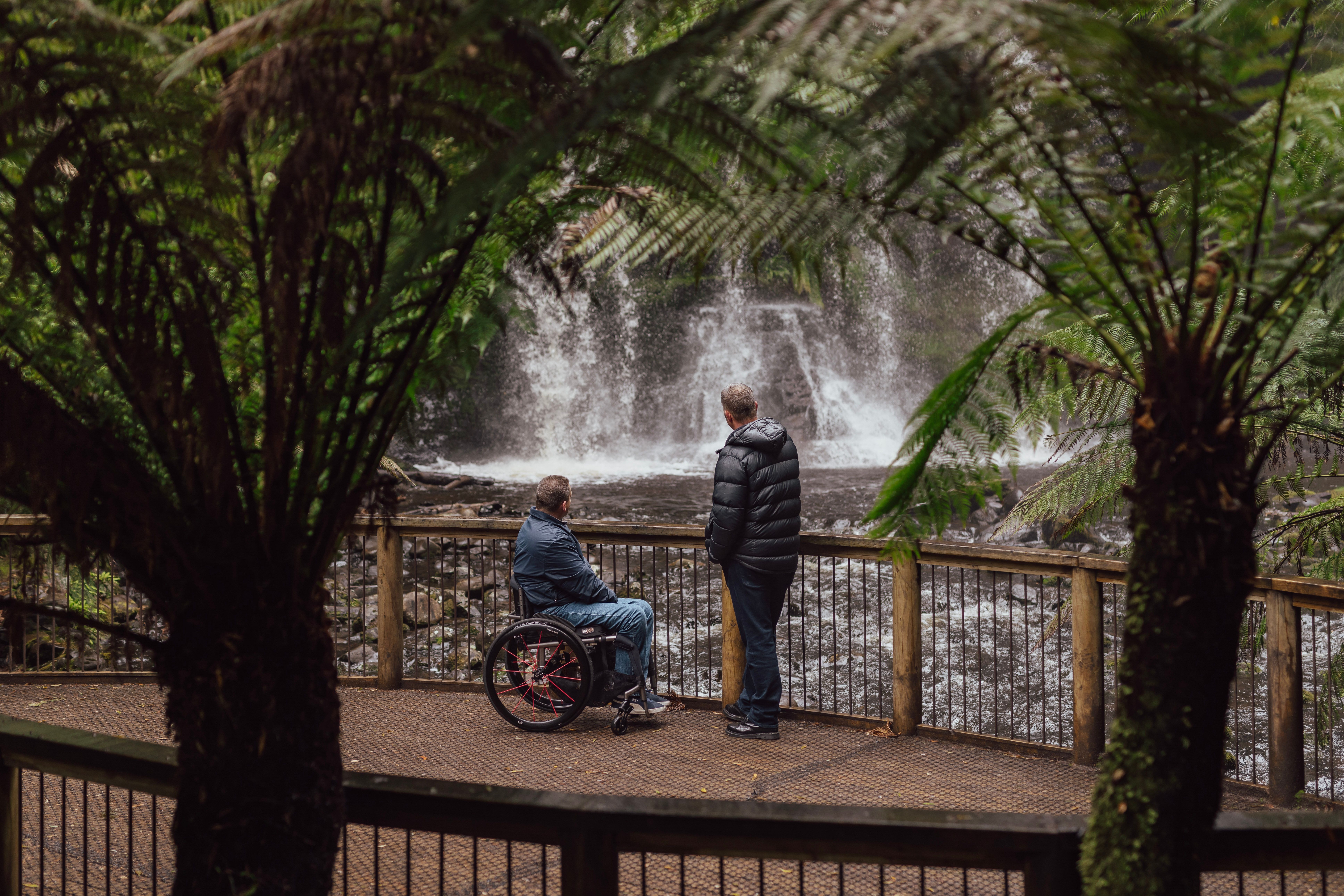 Two visitors view Russell Falls from an accessible viewing platform framed by vegetation at Mount Field National Park