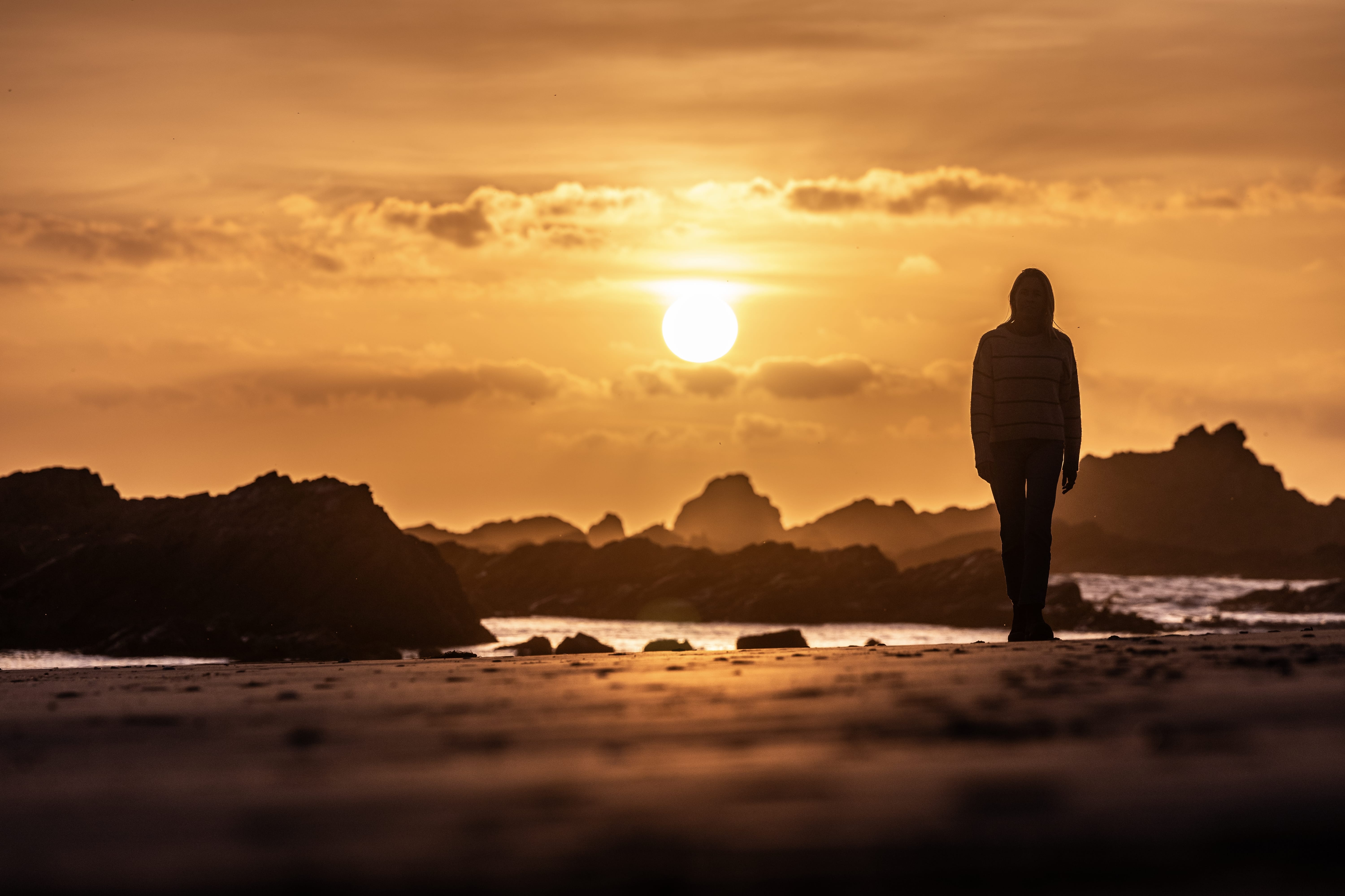 A person silhouetted on the beach at sunset with rocky outcrops at Arthur River, takayna / Tarkine