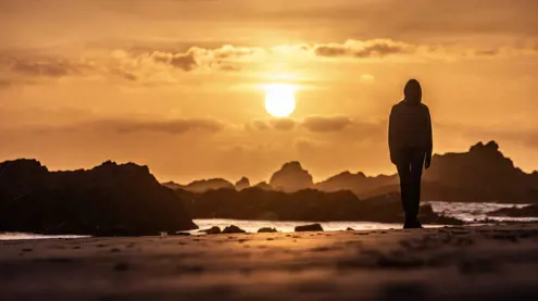 A person silhouetted on the beach at sunset with rocky outcrops at Arthur River, takayna / Tarkine