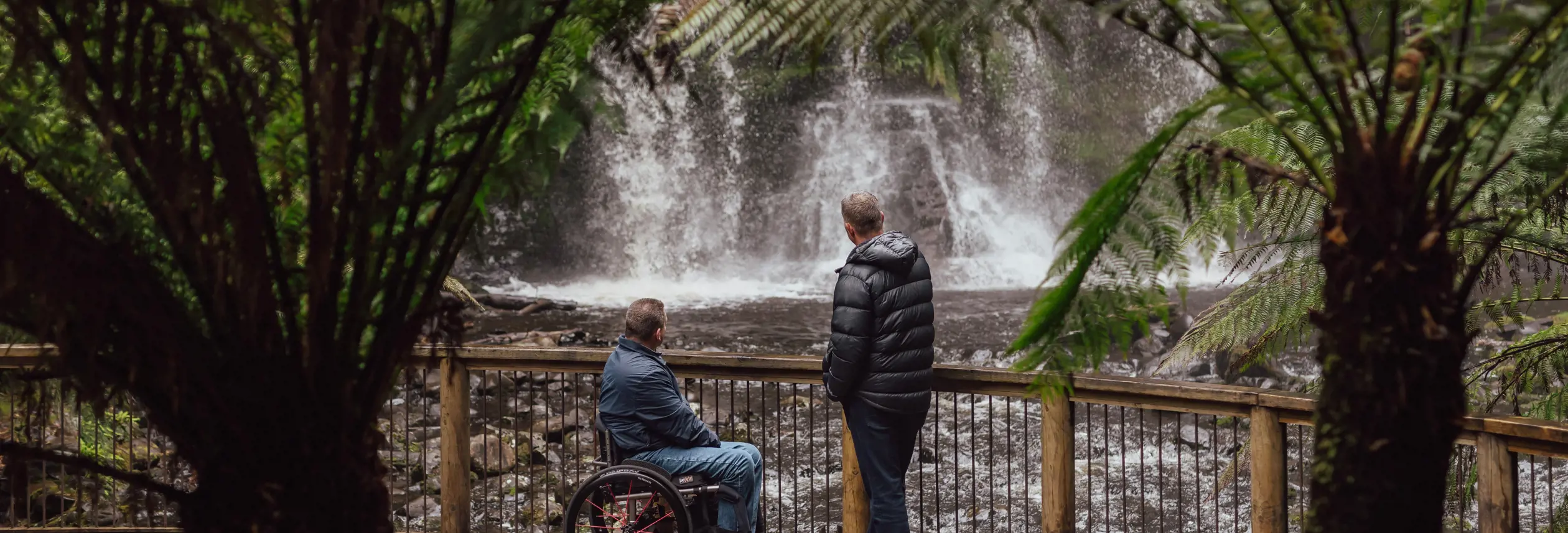 Two visitors view Russell Falls from an accessible viewing platform framed by vegetation at Mount Field National Park