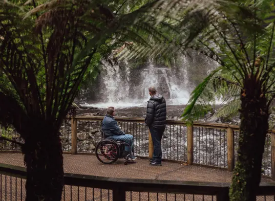Two visitors view Russell Falls from an accessible viewing platform framed by vegetation at Mount Field National Park
