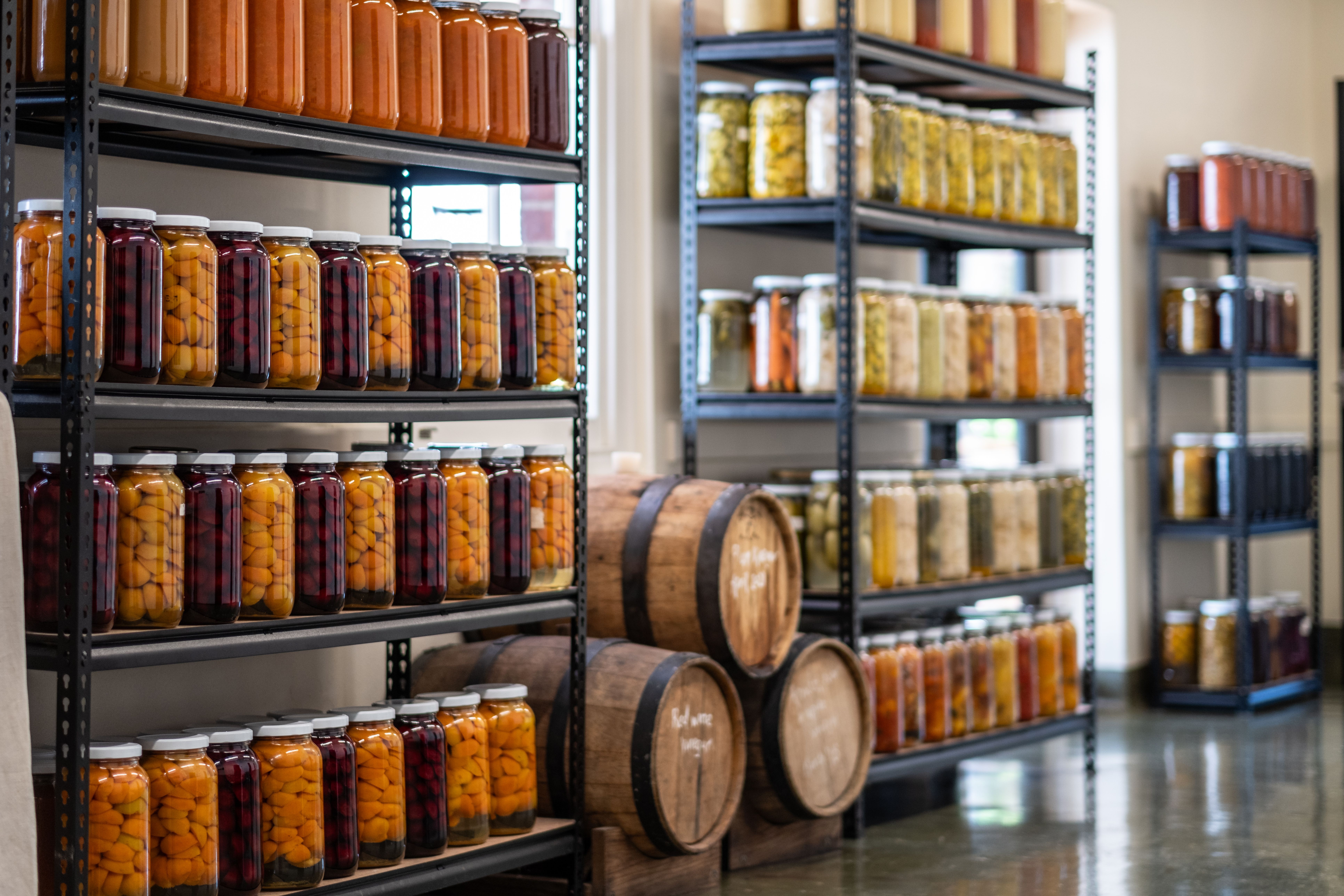 Shelves of preserved fruit and pickles in glass jars alongside wooden barrels at The Agrarian Kitchen in New Norfolk