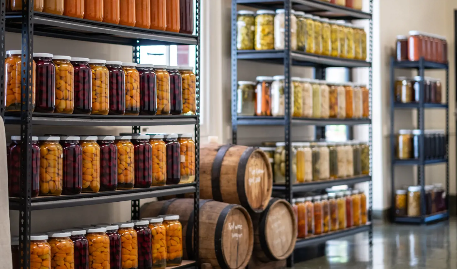 Shelves of preserved fruit and pickles in glass jars alongside wooden barrels at The Agrarian Kitchen in New Norfolk