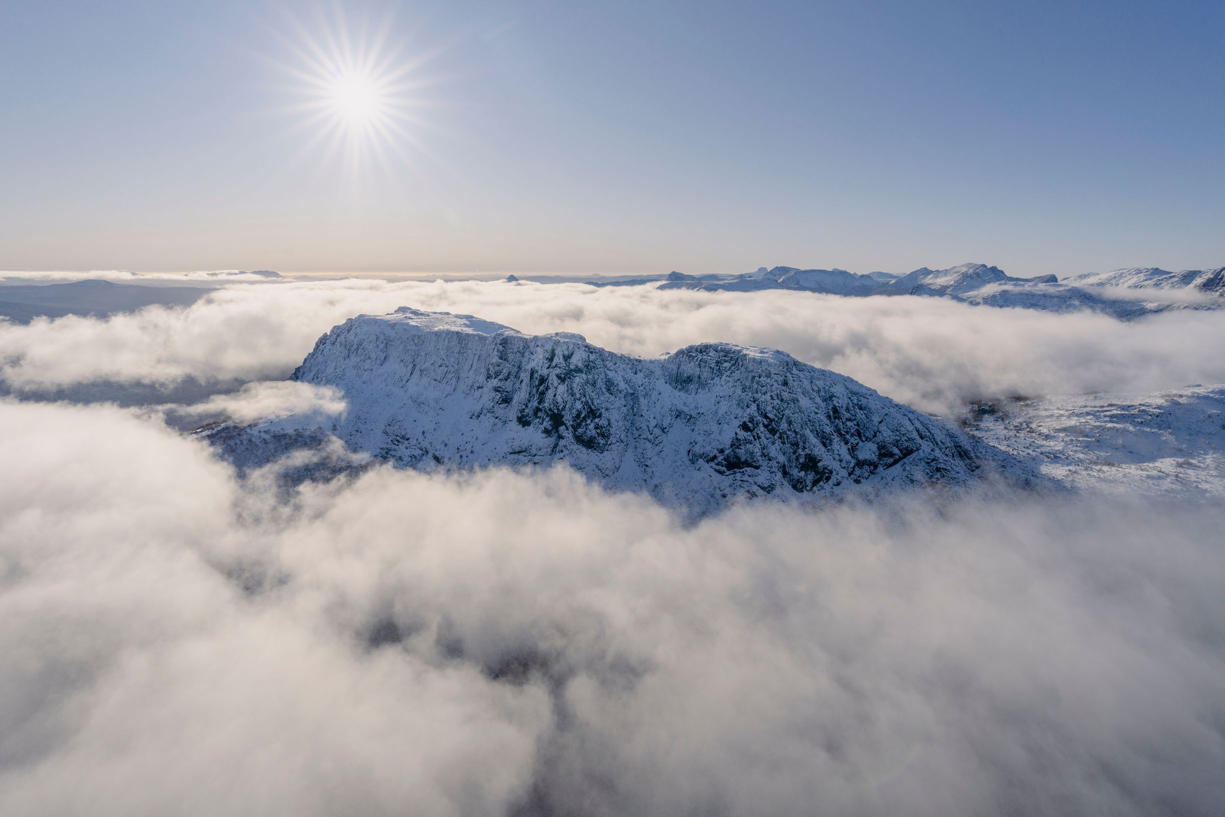 Aerial view of snow covered High Dome in The Eldons rising above a sea of clouds with a sunburst in a clear sky