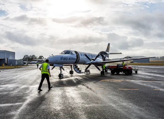 Ground crew in high visibility vests working around a Sharp Airlines propeller aircraft on a wet tarmac, King Island Airport