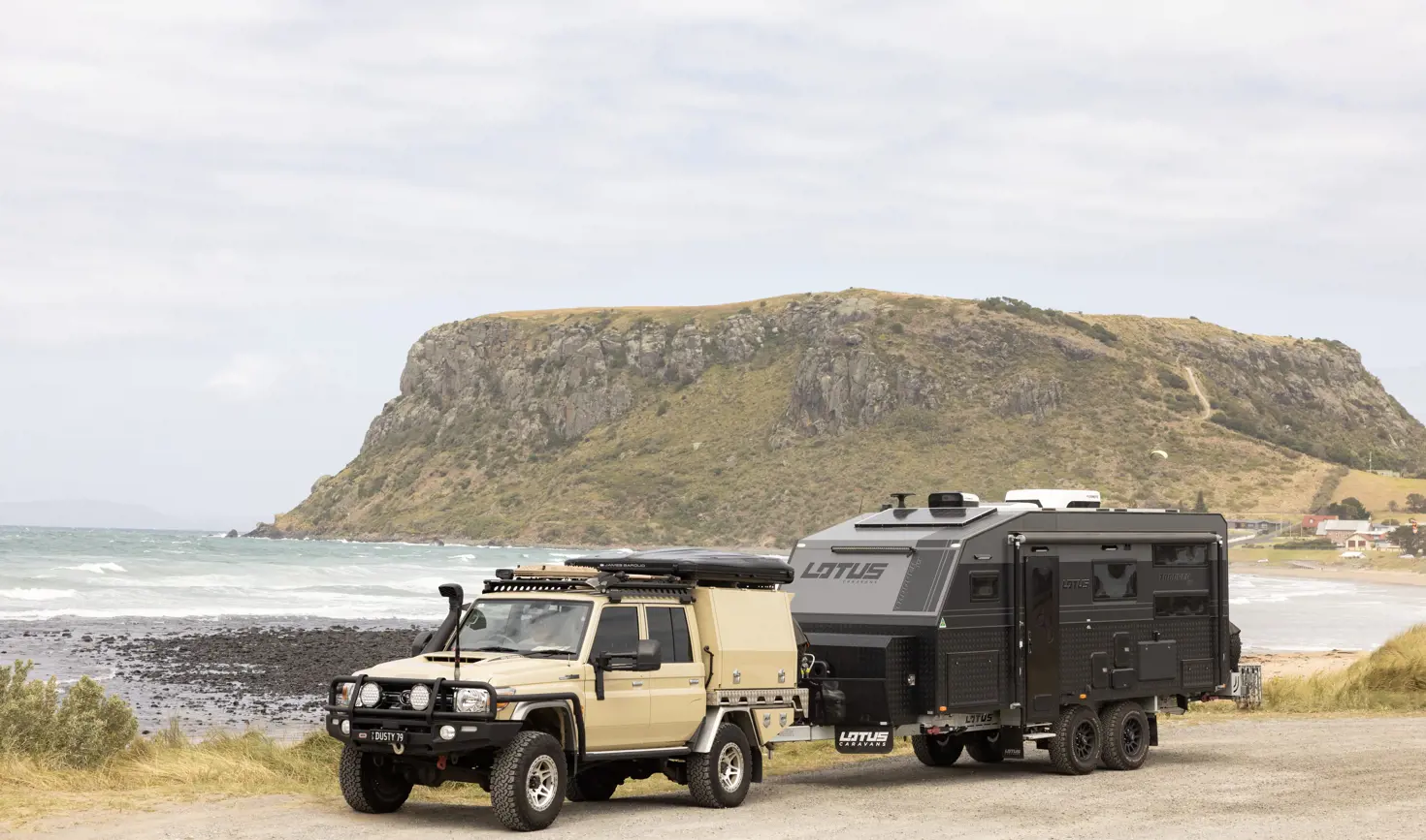 A 4WD towing a Lotus caravan parked on the foreshore with The Nut and the beach beyond, Stanley