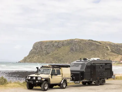 A 4WD towing a Lotus caravan parked on the foreshore with The Nut and the beach beyond, Stanley