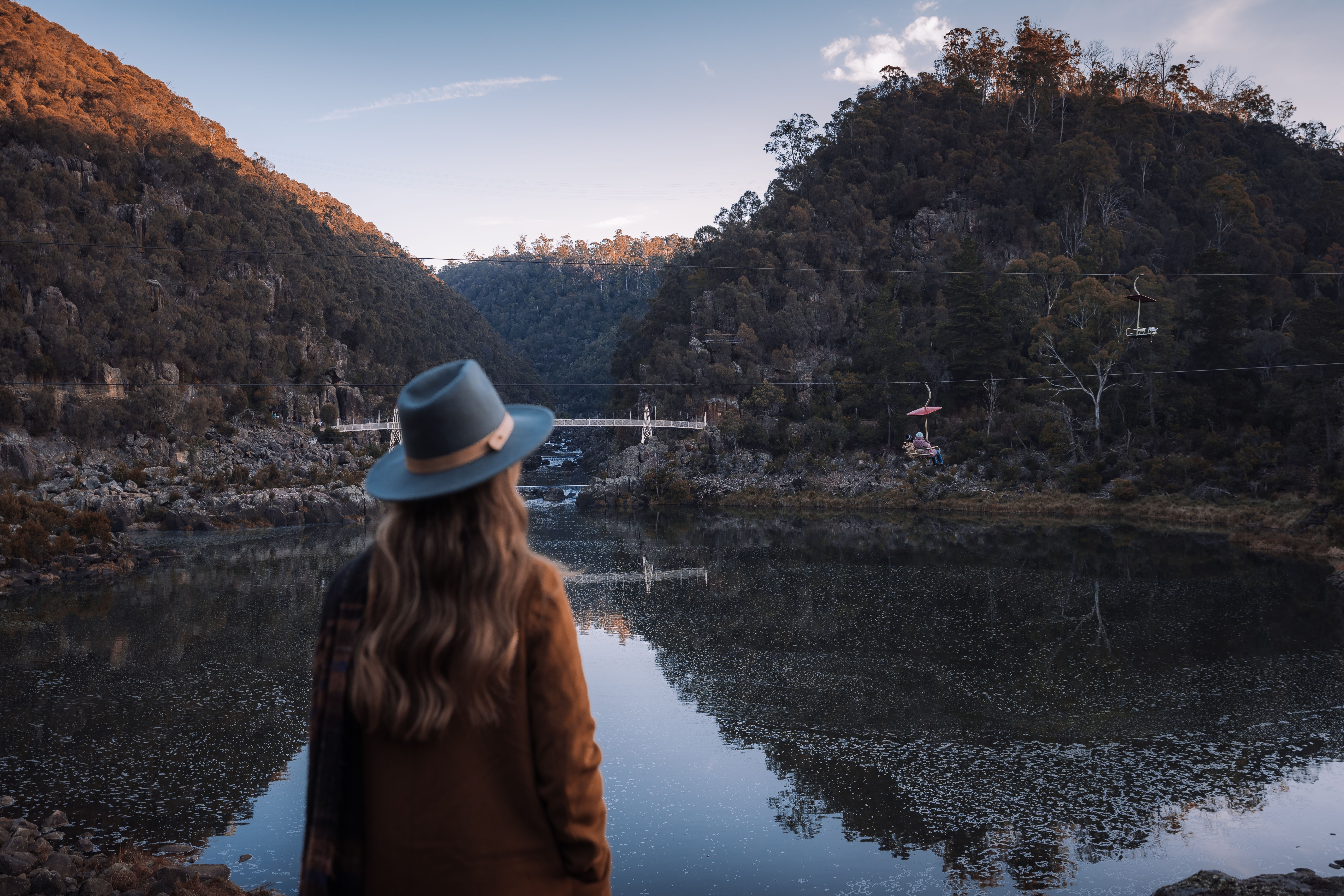 A person in a wide brim hat takes in the view across the still water of Cataract Gorge Reserve, Launceston