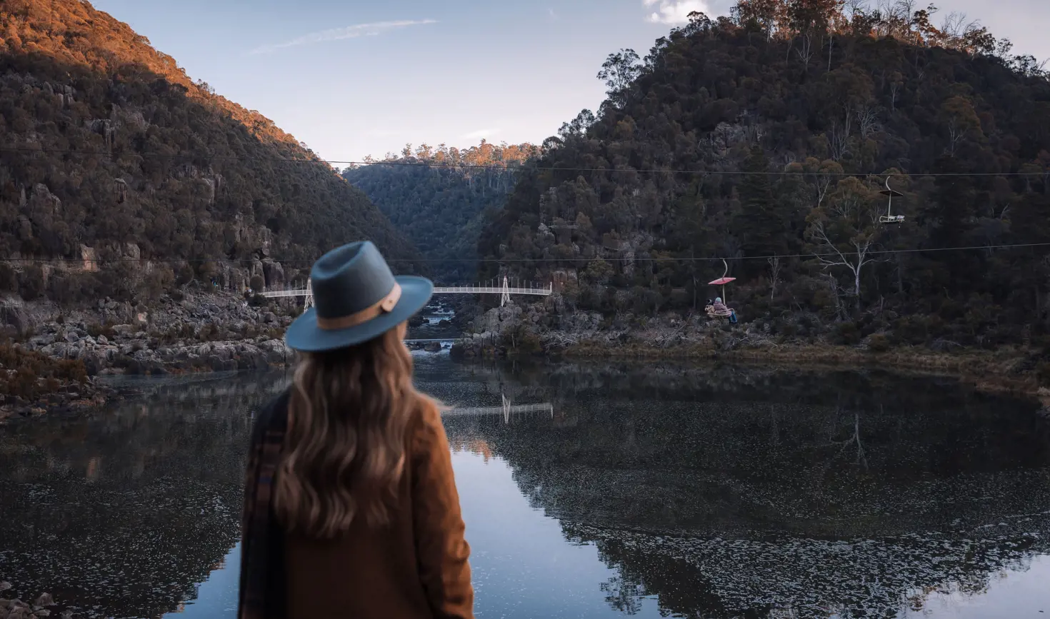 A person in a wide brim hat takes in the view across the still water of Cataract Gorge Reserve, Launceston