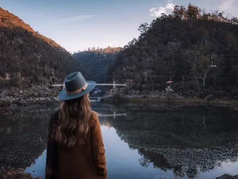 A person in a wide brim hat takes in the view across the still water of Cataract Gorge Reserve, Launceston