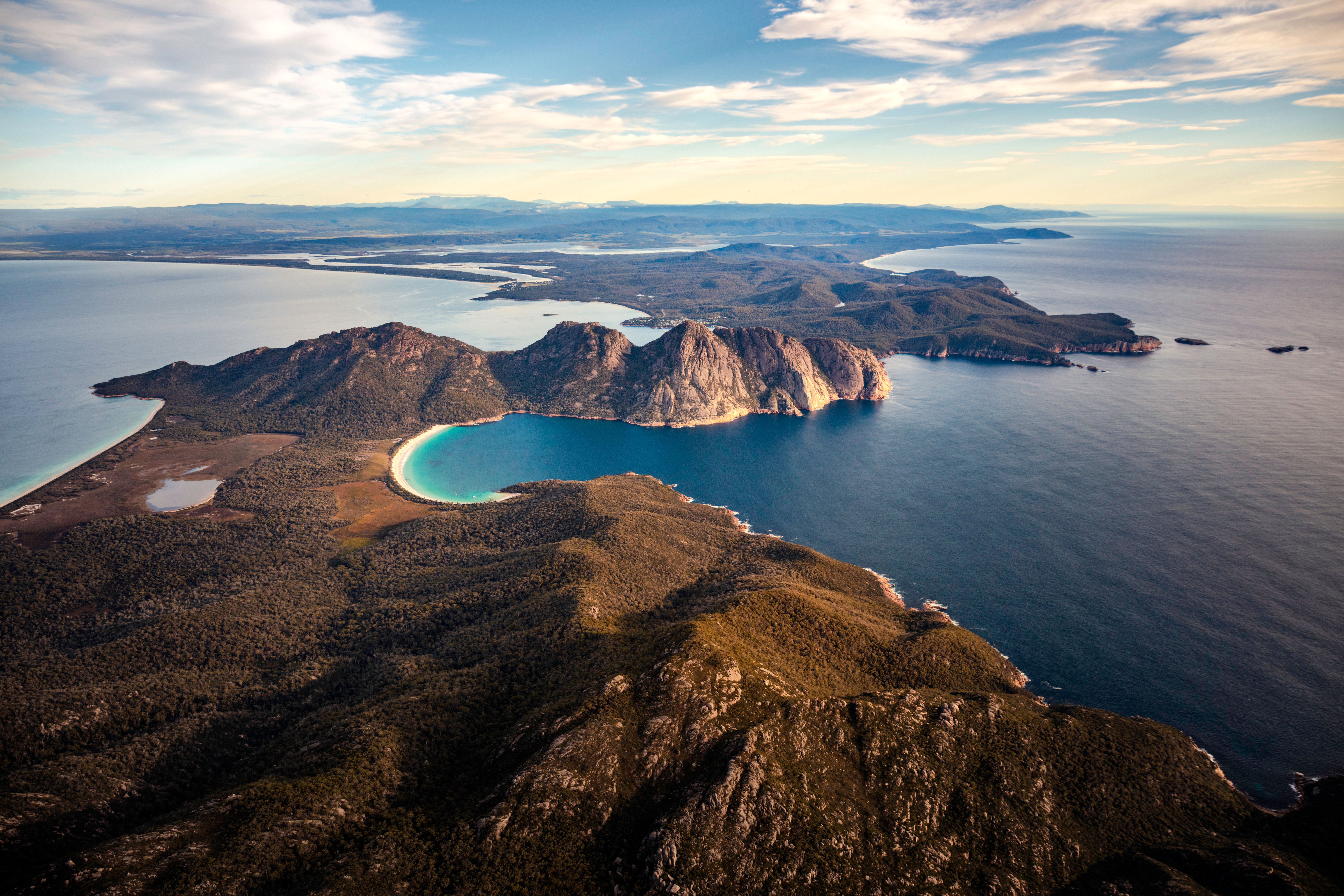 Aerial view of Wineglass Bay's crescent beach and turquoise water flanked by coastal cliffs, Freycinet National Park
