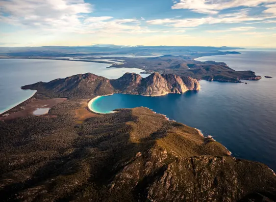 Aerial view of Wineglass Bay's crescent beach and turquoise water flanked by coastal cliffs, Freycinet National Park