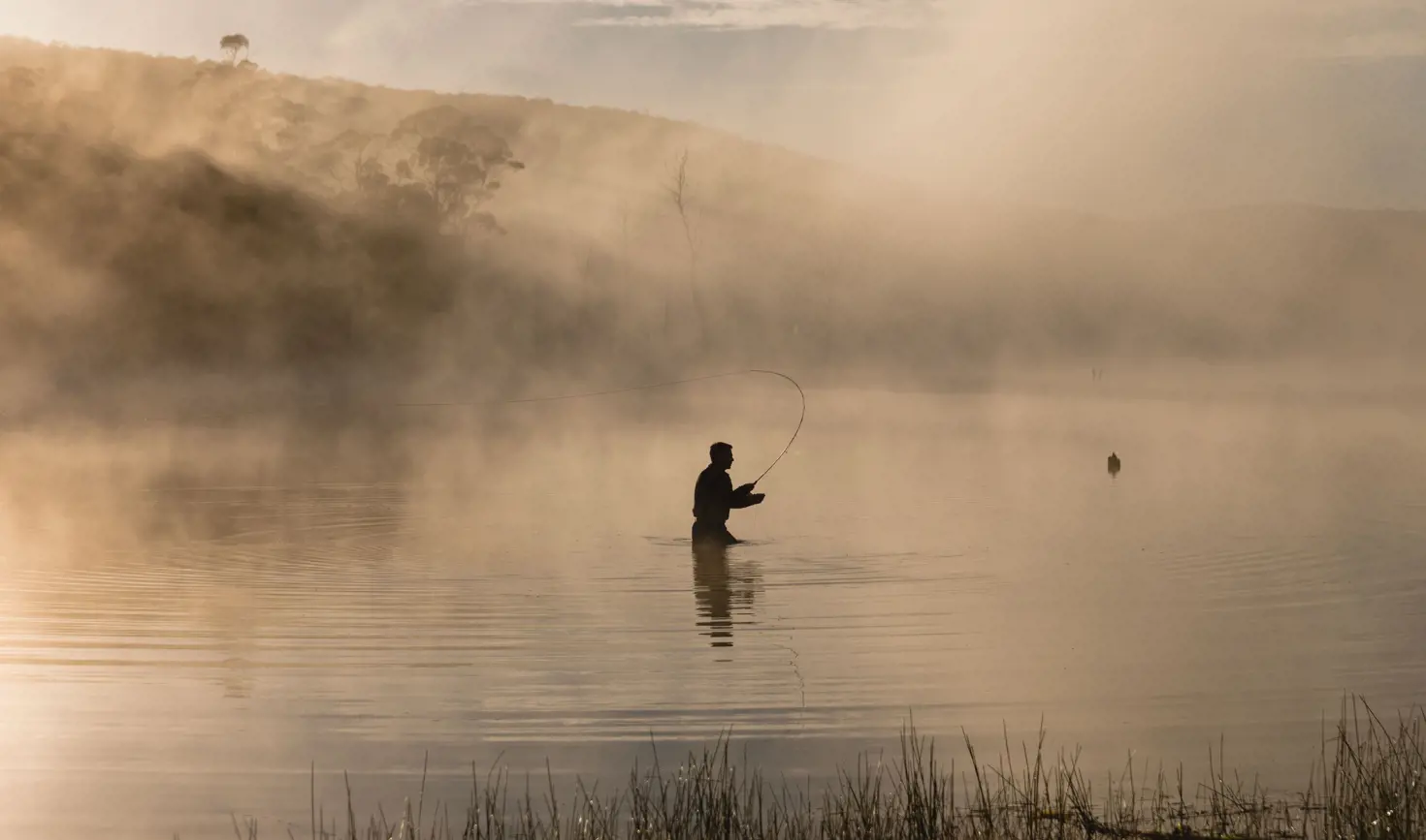 Silhouette of a fly fisher casting on misty Lake Leake, Tasmania's east coast