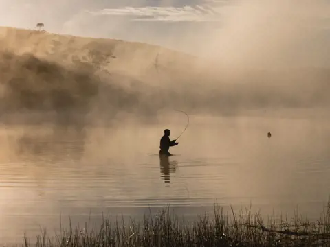 Silhouette of a fly fisher casting on misty Lake Leake, Tasmania's east coast