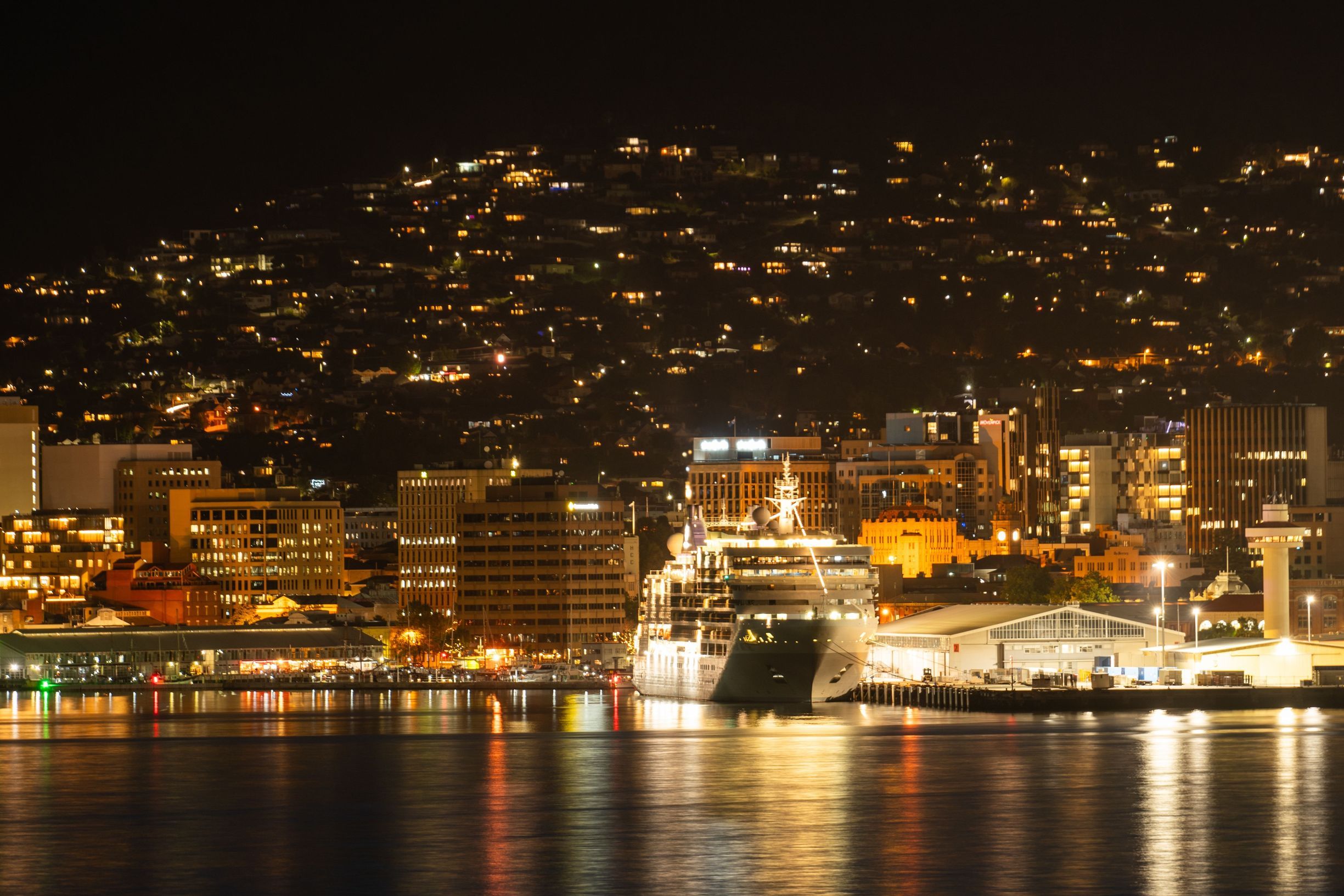 Silver Muse cruise ship docked at Hobart Port at night with the city lights reflected on the water