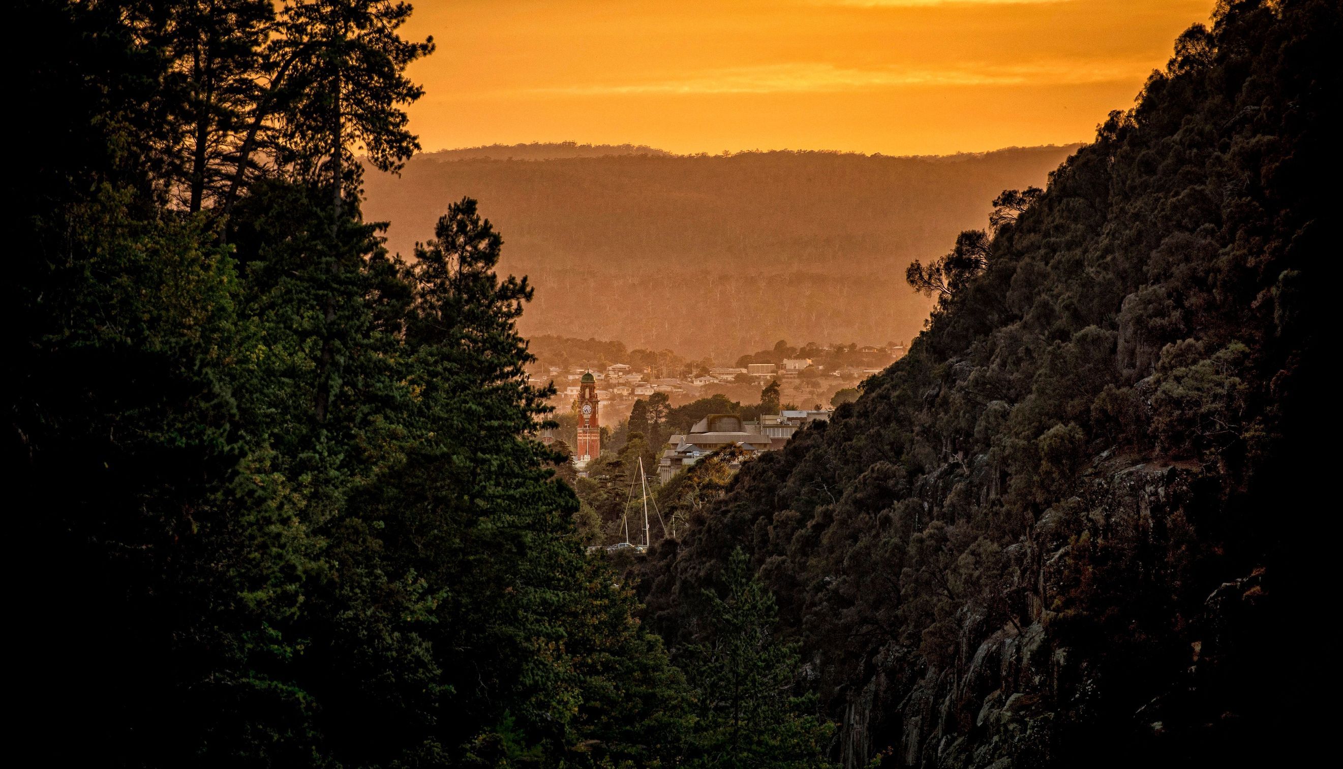 Cataract Gorge view at sunrise toward Launceston with a clock tower visible through bushland framing