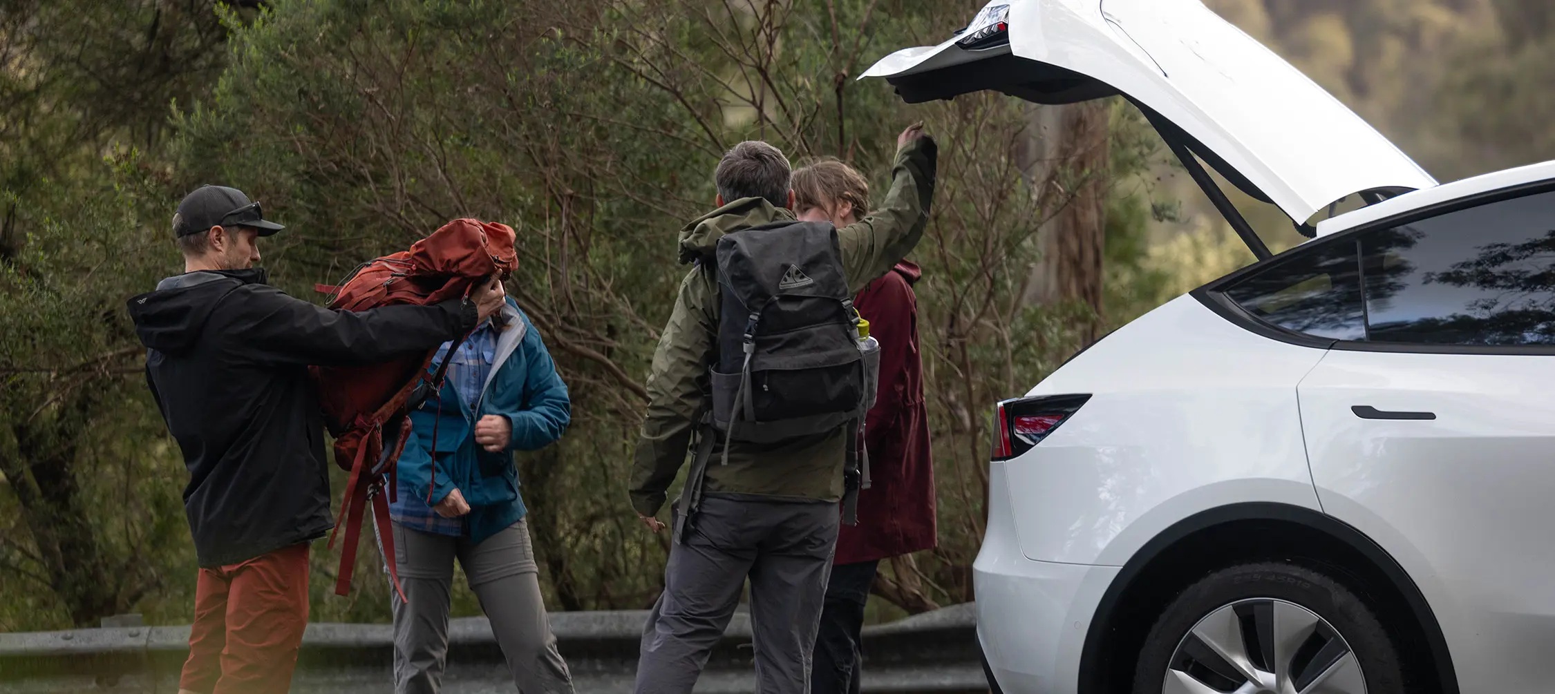 Group of hikers loading backpacks into a hire car boot for a Tasmania road trip