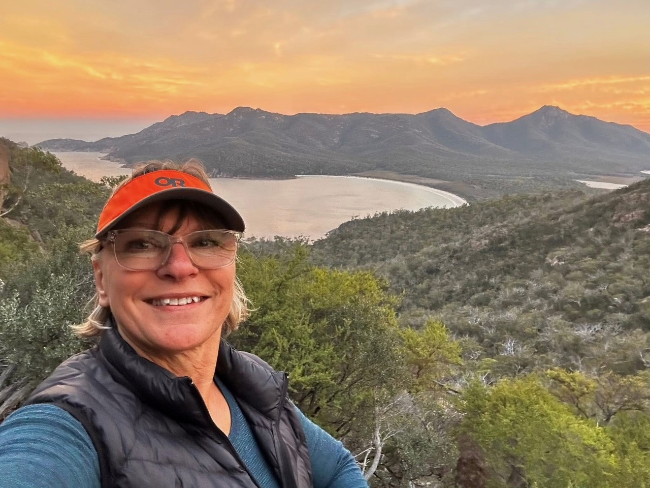 Karen Stotz at a lookout above a curved beach and bay with a mountain range in the distance