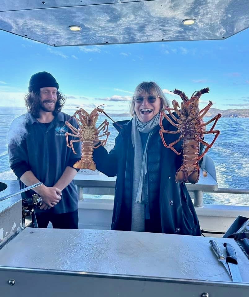 Karen Stotz holding two rock lobsters with a crew member aboard a boat at sea