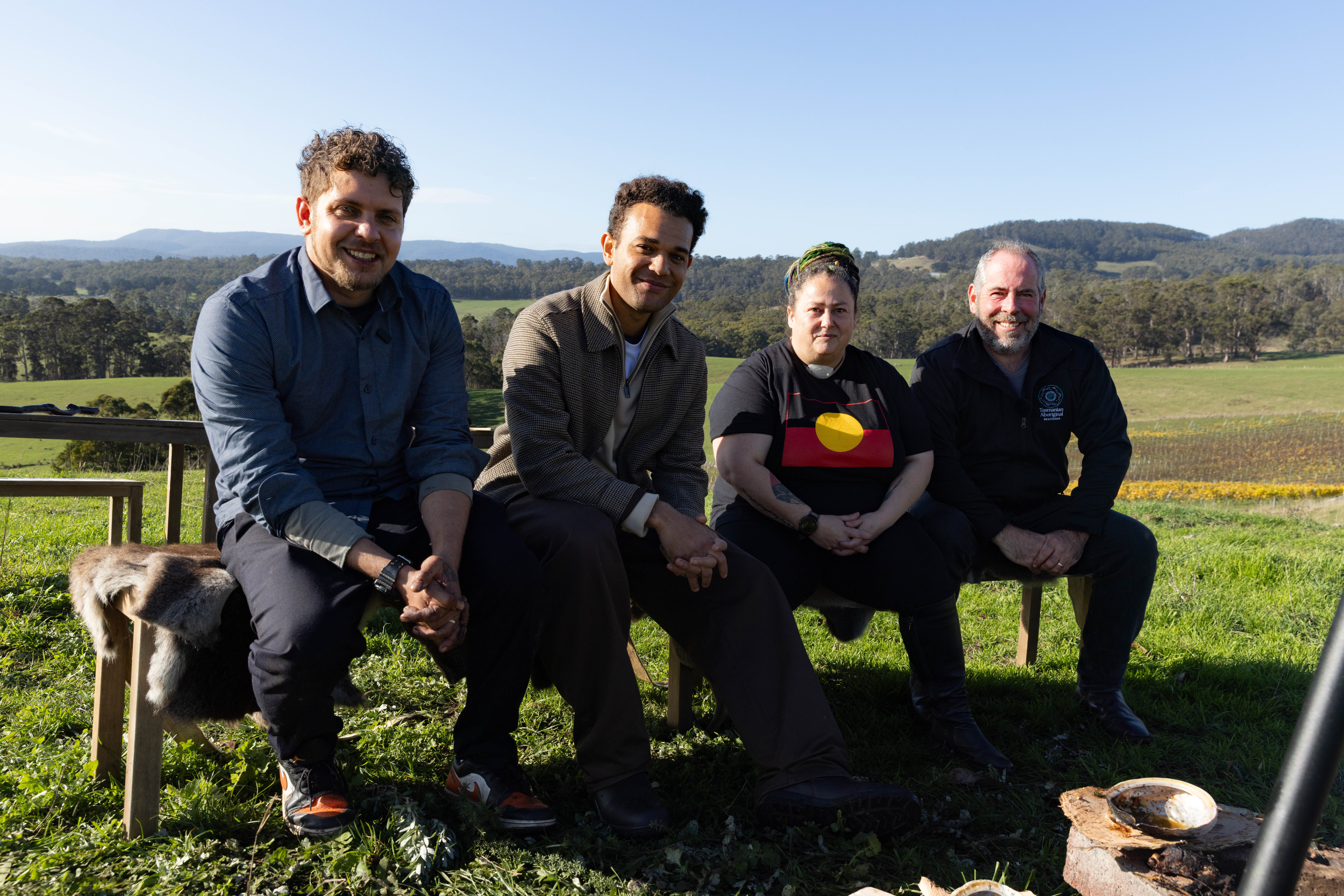 Djuker Hart, presenter Zev Ryall, Trish Hodge and Daniel Kelleher seated on a bench in a grassy field with hills beyond
