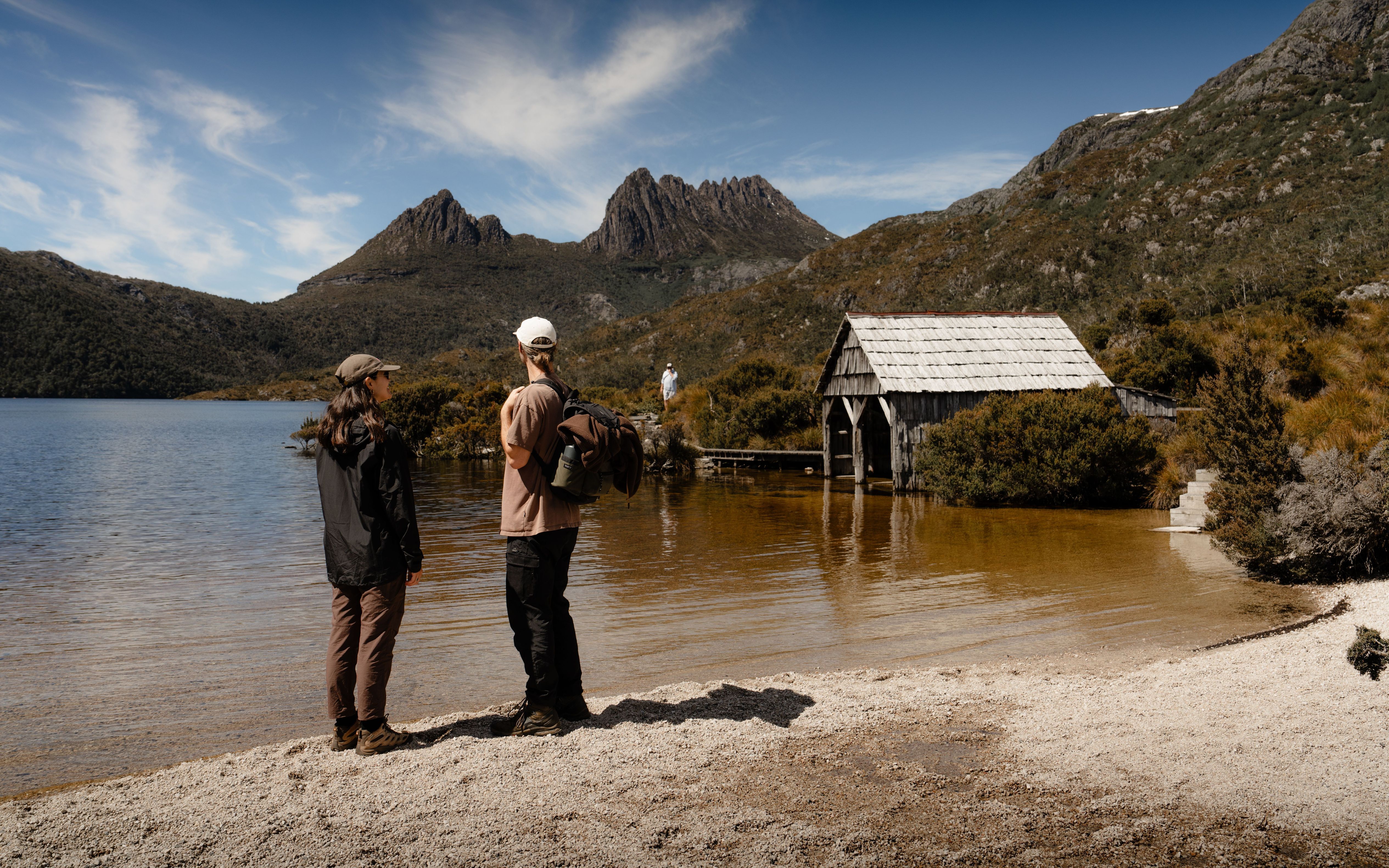 Two walkers looking across Dove Lake towards Cradle Mountain with the historic boat shed, Cradle Mountain-Lake St Clair National Park