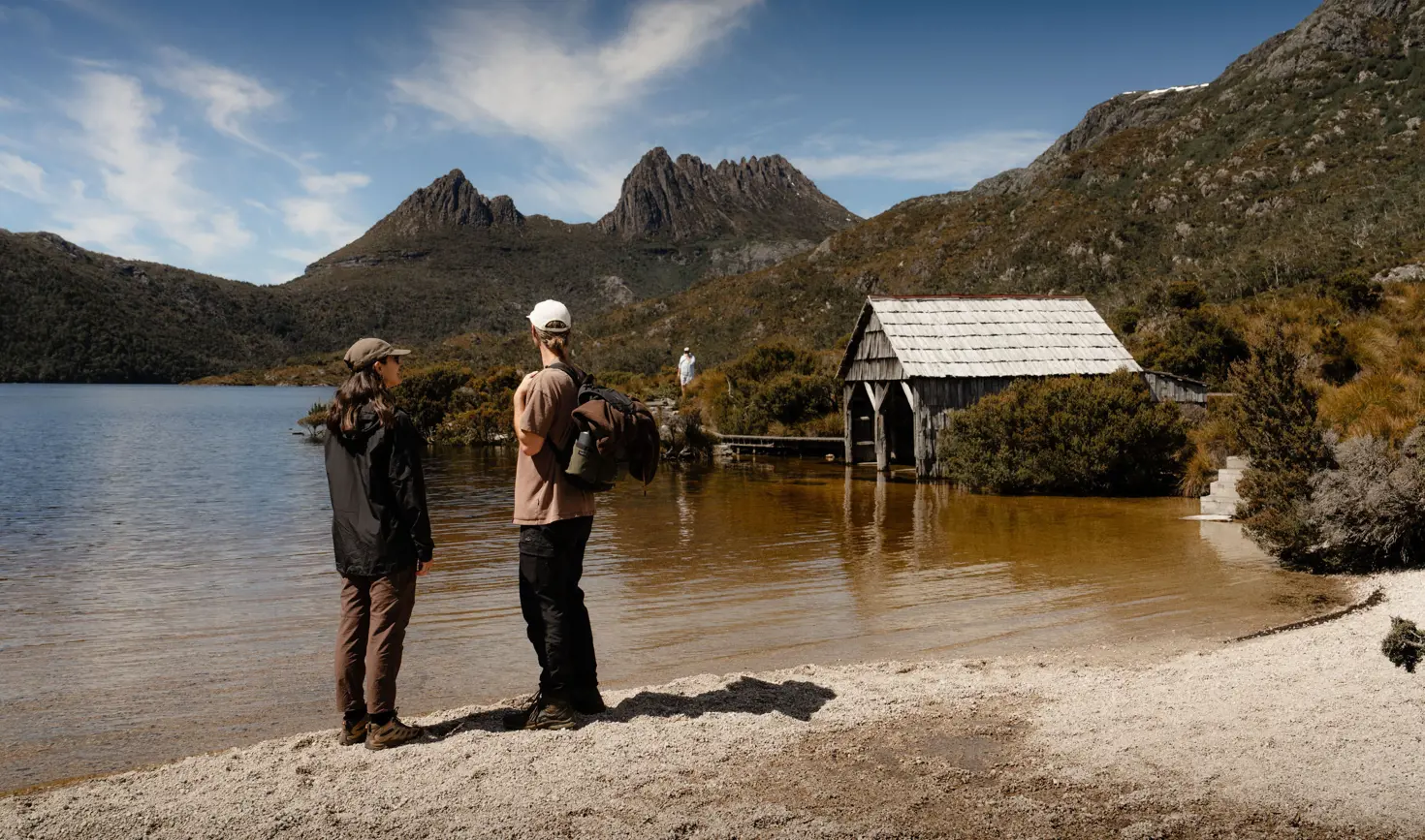 Two walkers looking across Dove Lake towards Cradle Mountain with the historic boat shed, Cradle Mountain-Lake St Clair National Park
