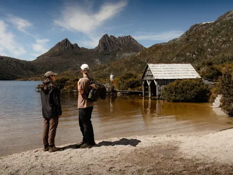 Two walkers looking across Dove Lake towards Cradle Mountain with the historic boat shed, Cradle Mountain-Lake St Clair National Park