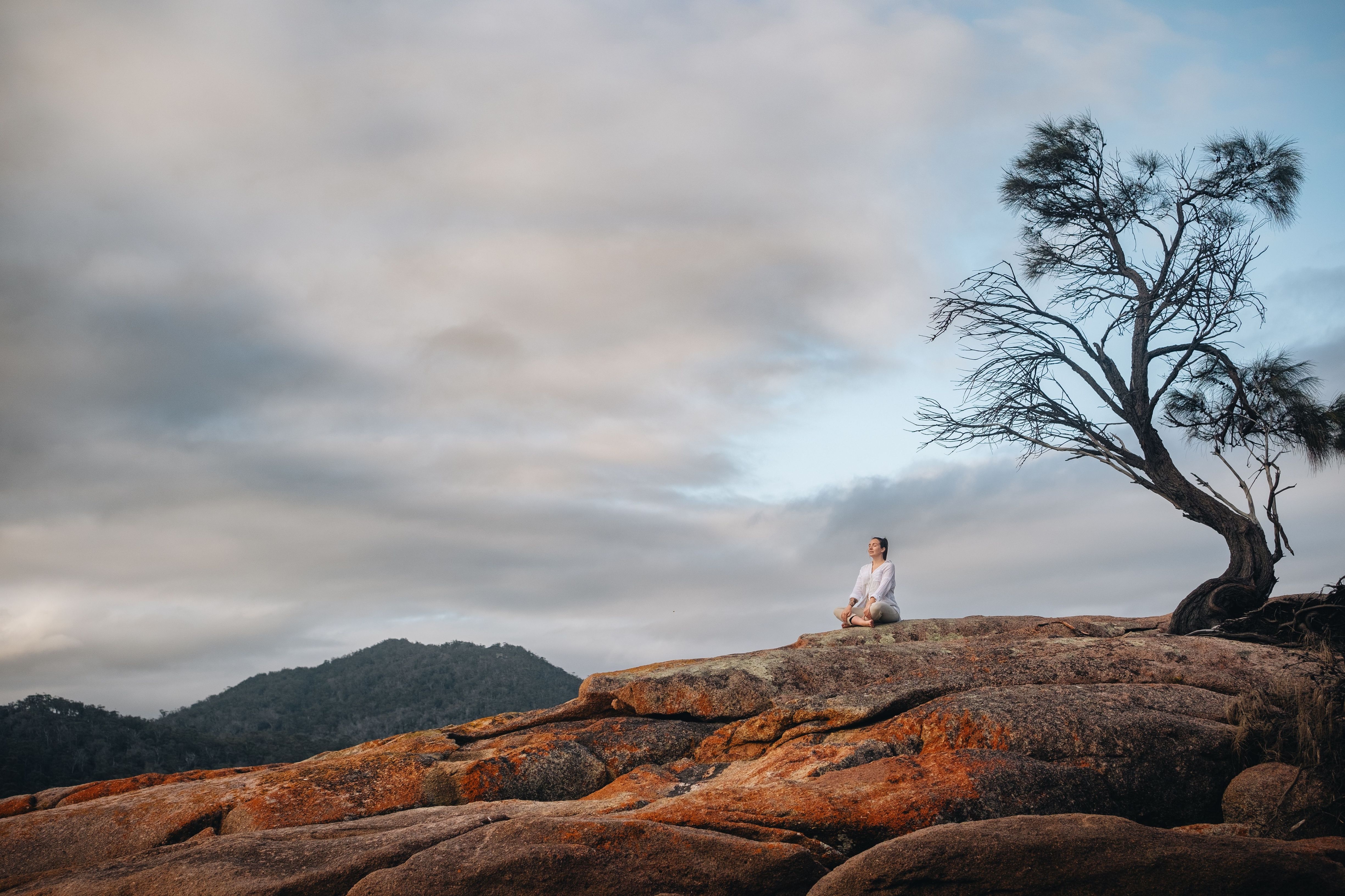 Person sitting cross-legged on the orange lichen-covered granite rocks at Honeymoon Bay, Freycinet National Park, Tasmania