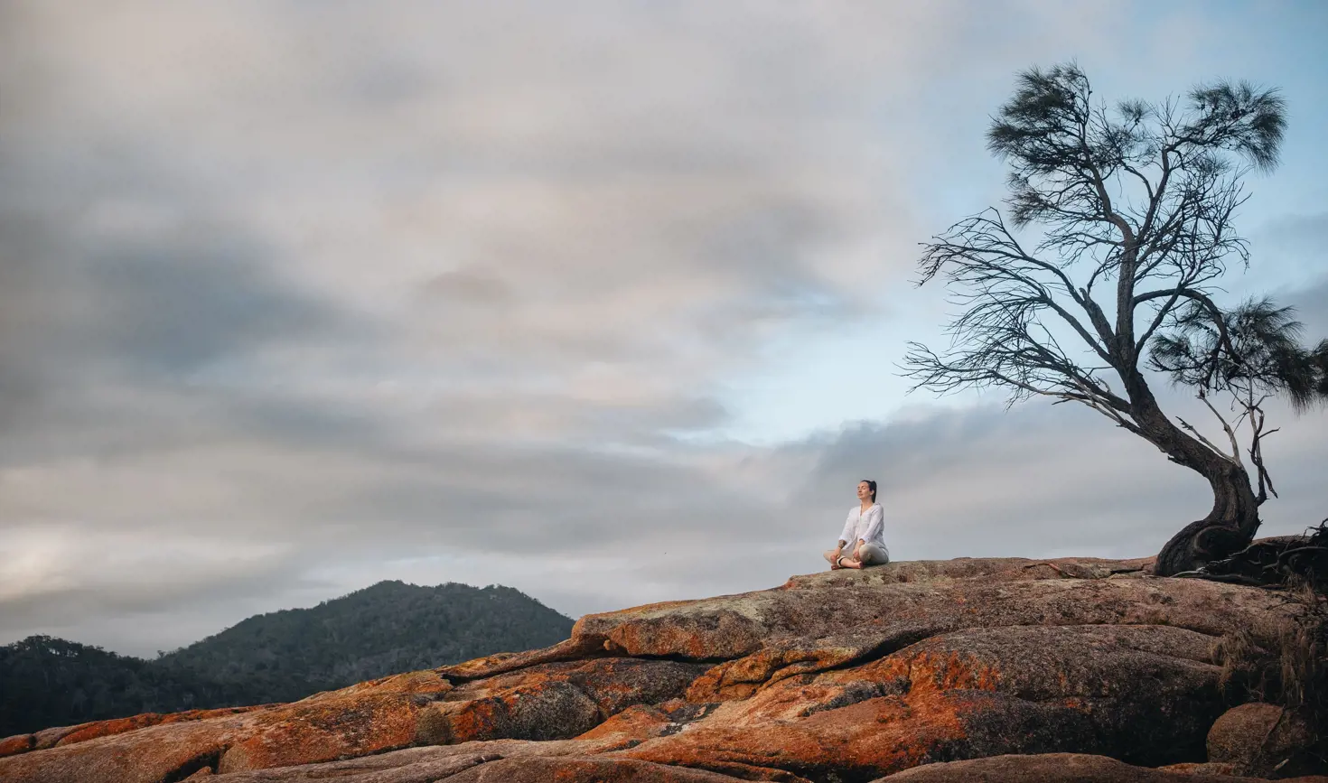 Person sitting cross-legged on the orange lichen-covered granite rocks at Honeymoon Bay, Freycinet National Park, Tasmania