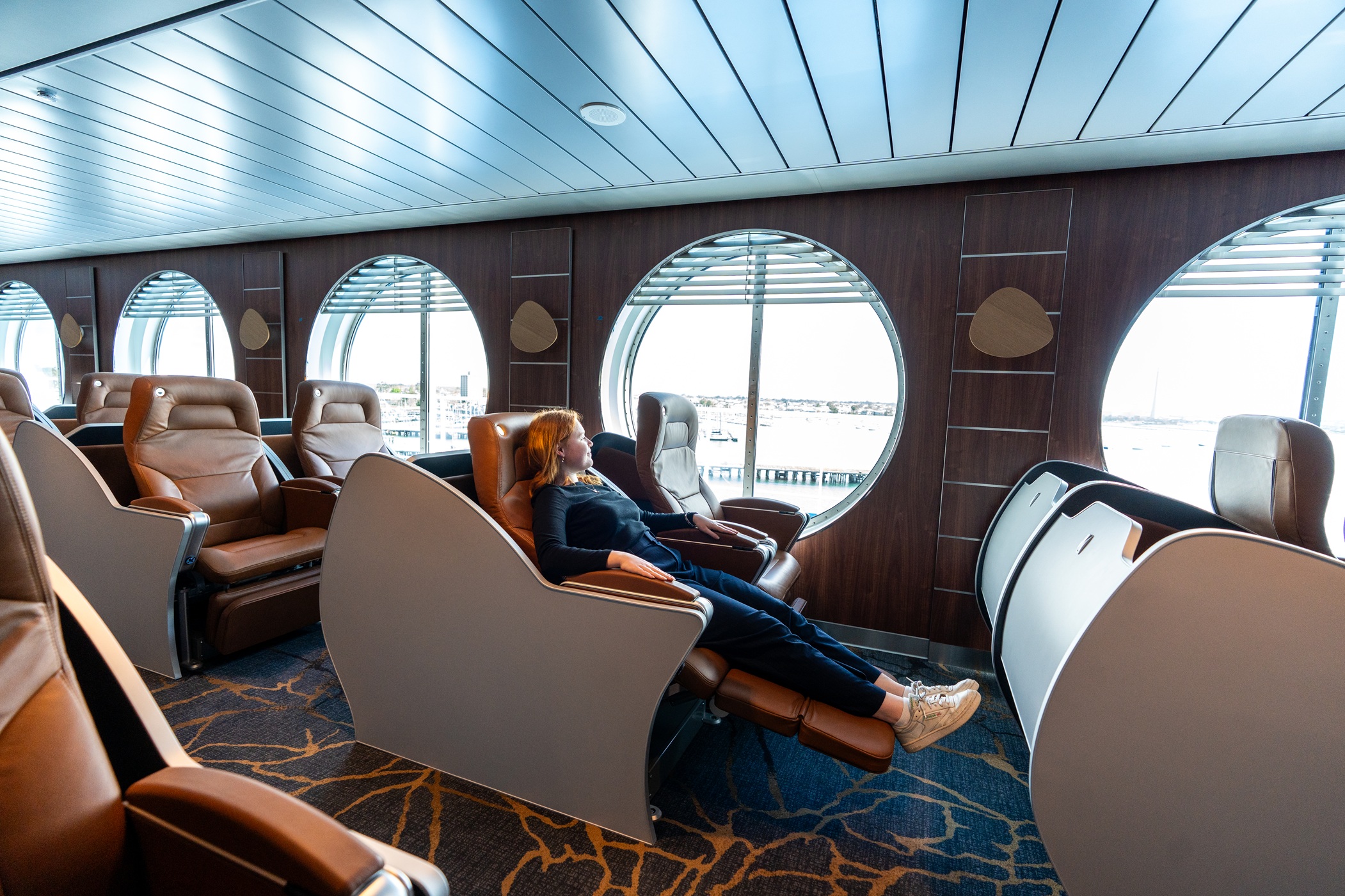 Person reclining in a lounge seat by a porthole window on Spirit of Tasmania