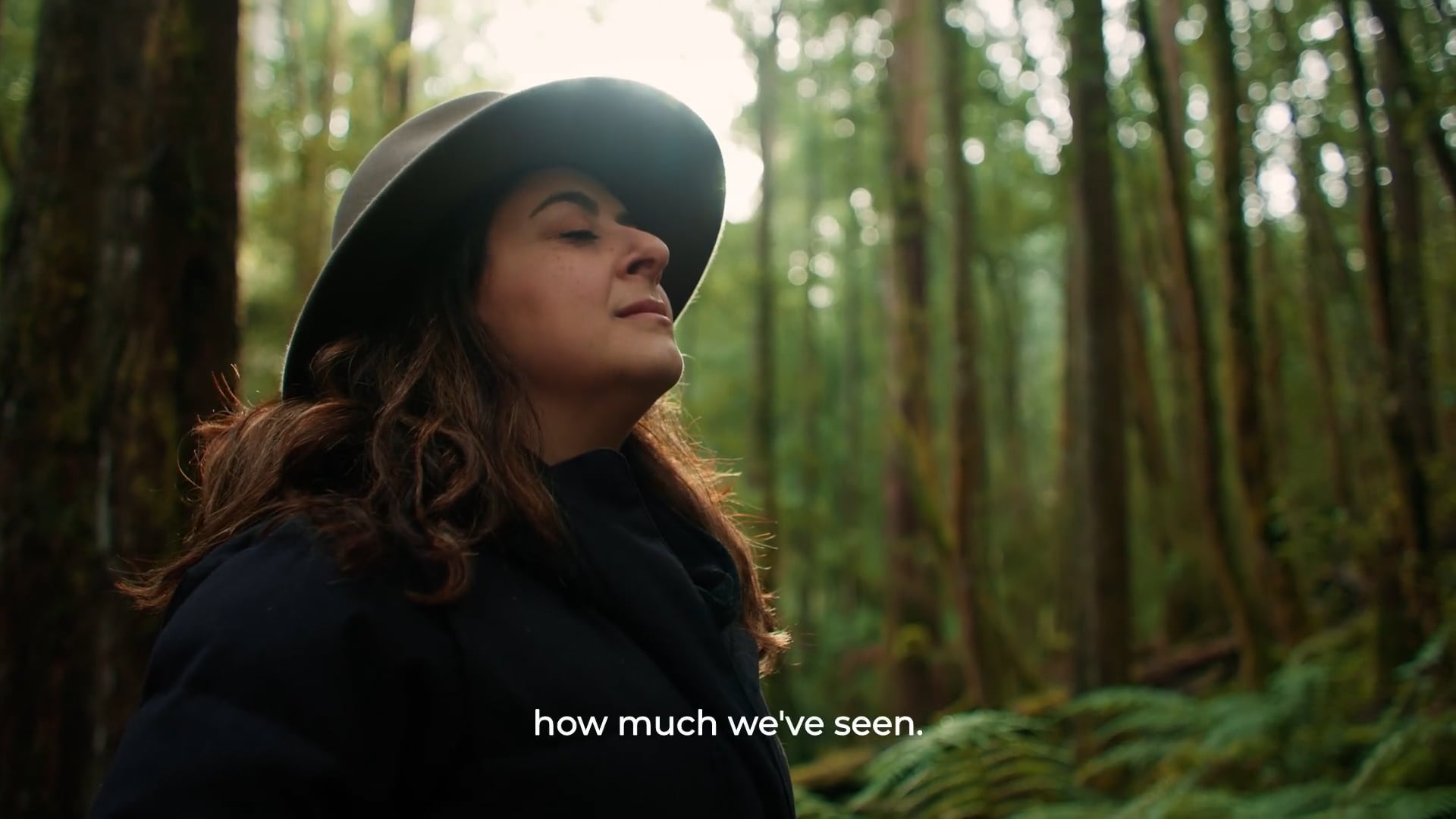 Susie Youssef standing with eyes closed among tall mossy forest trees on an Intrepid Travel tour of Tasmania