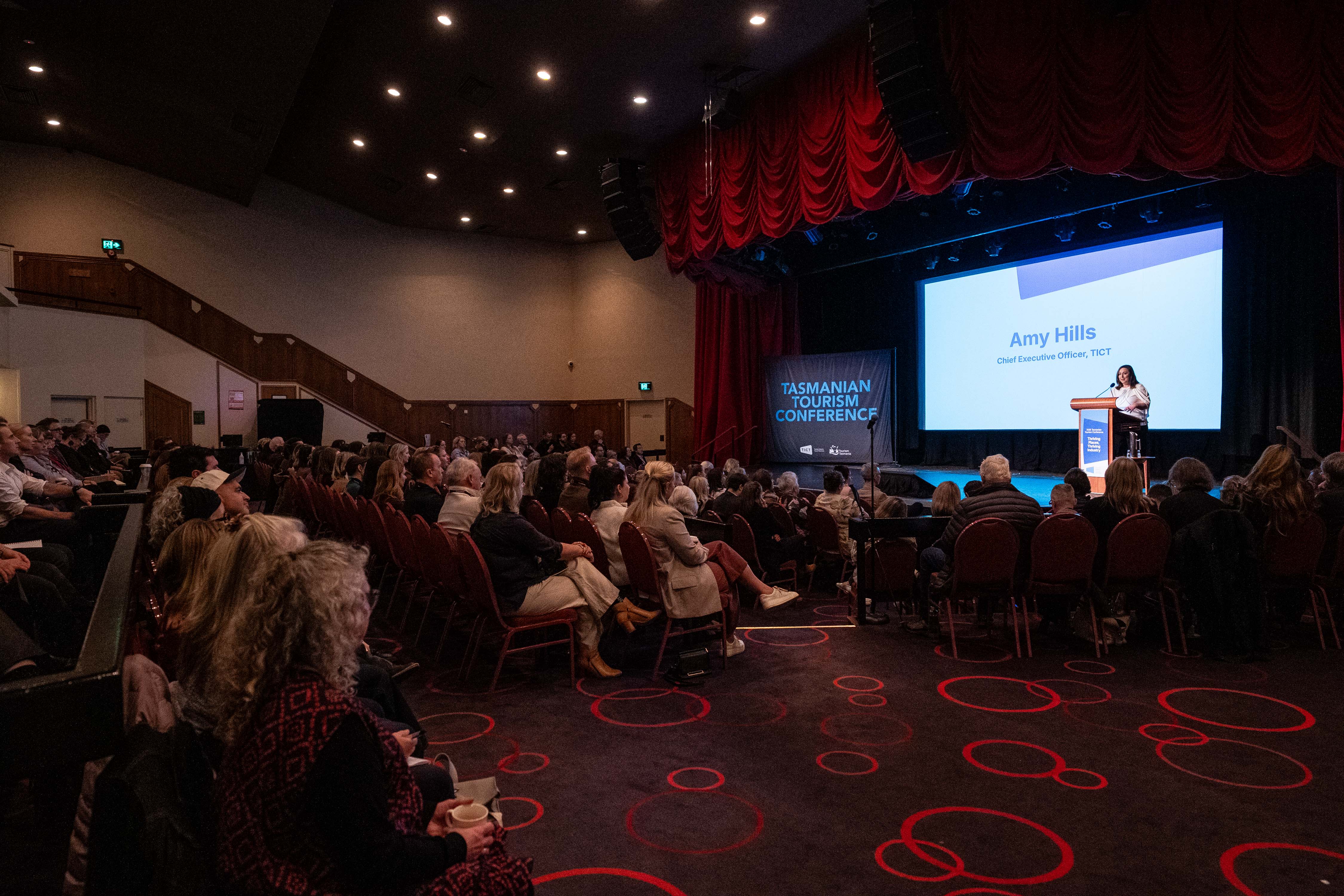 Amy Hills, CEO of TICT, speaking at a podium to a seated audience at the Tasmanian Tourism Conference, Launceston