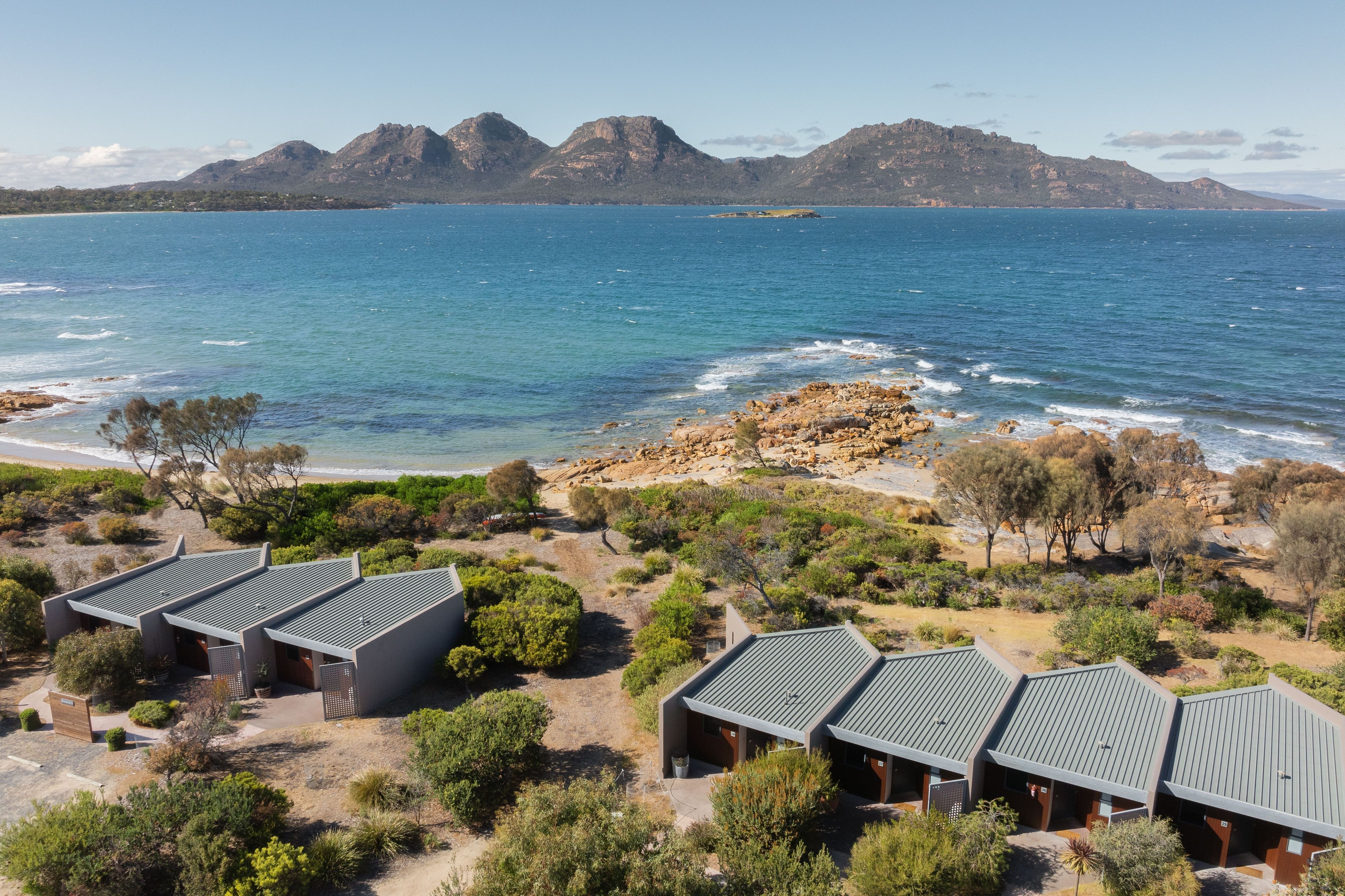 Aerial view of Edge of the Bay Resort cabins by the coast with mountains across the bay at Coles Bay, east coast