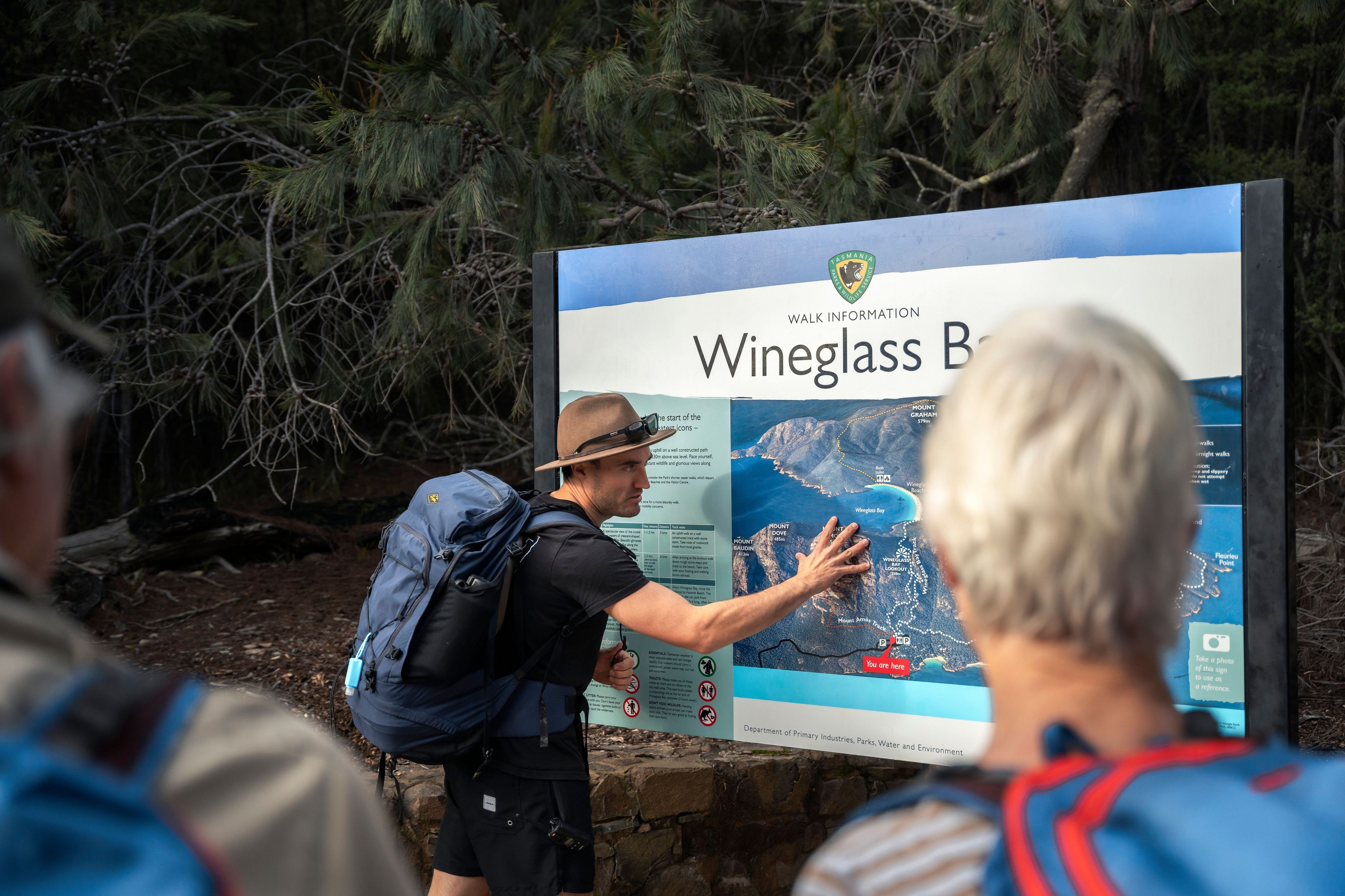 Guide pointing to a Wineglass Bay walk information sign for hikers on a Freycinet Walking Tour, Freycinet National Park