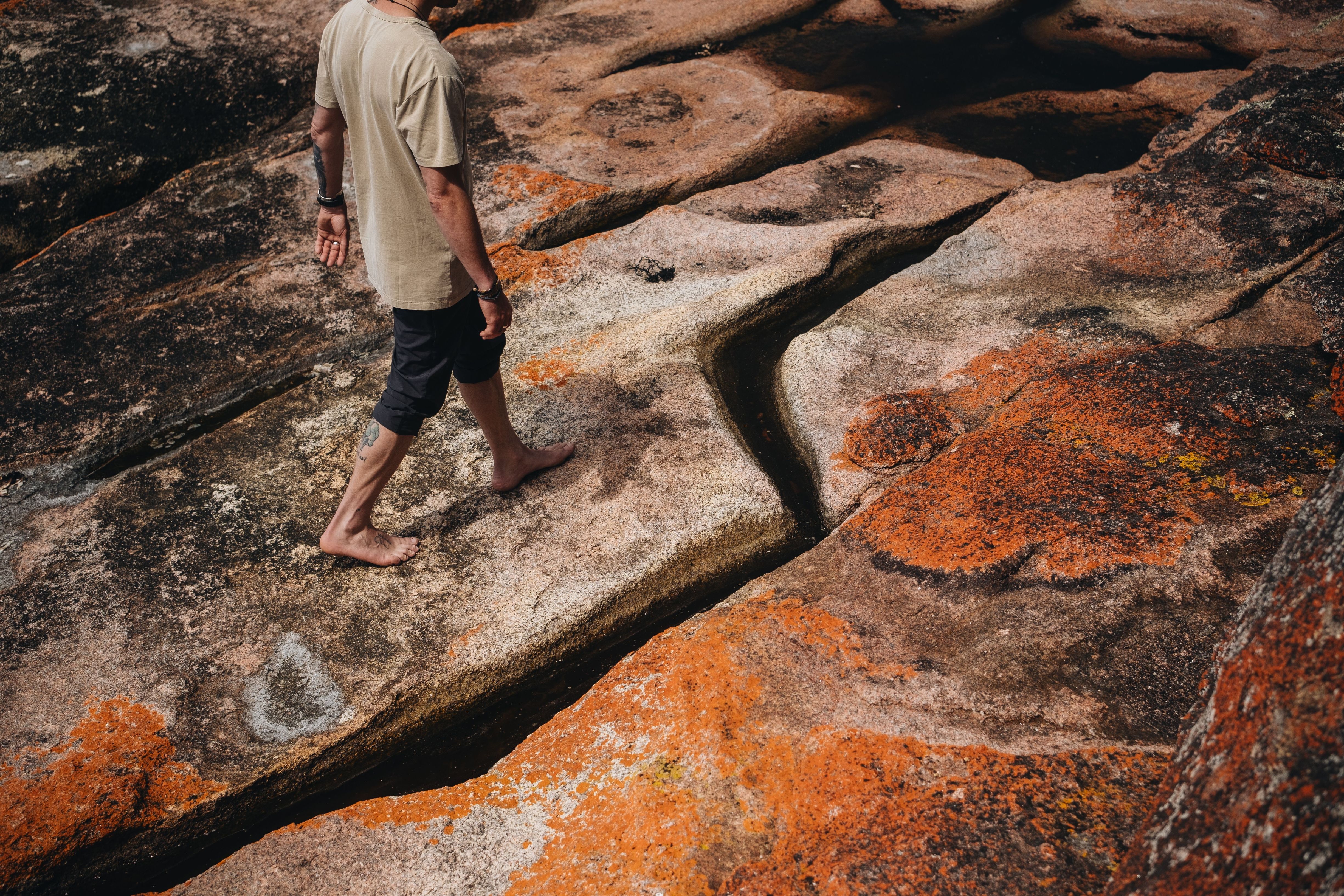 Person walking barefoot across orange lichen-covered granite rocks at Sleepy Bay, Freycinet National Park
