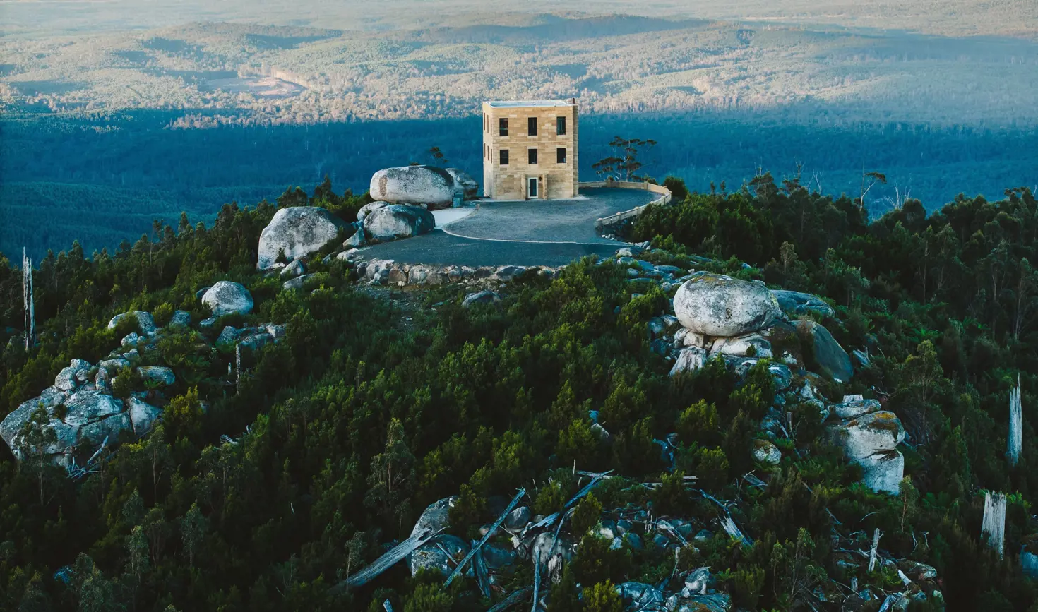 Aerial view of a sandstone tower building perched among granite boulders on a forested hilltop at The Keep in Goulds Country