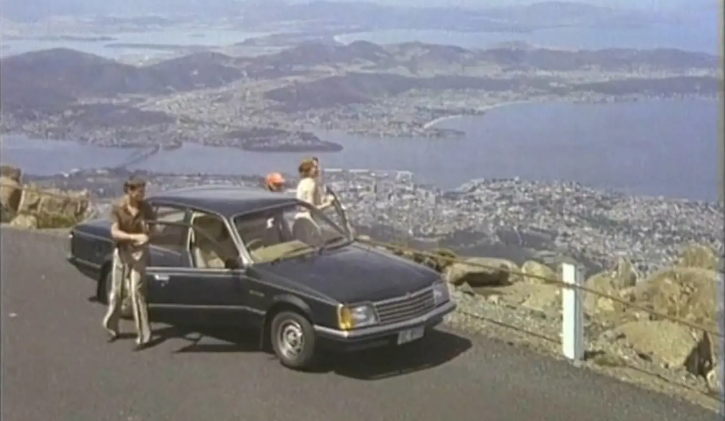 Video screengrab from the 1980 Freewheelin' around Tasmania campaign with travellers and a car overlooking Hobart from kunanyi / Mount Wellington