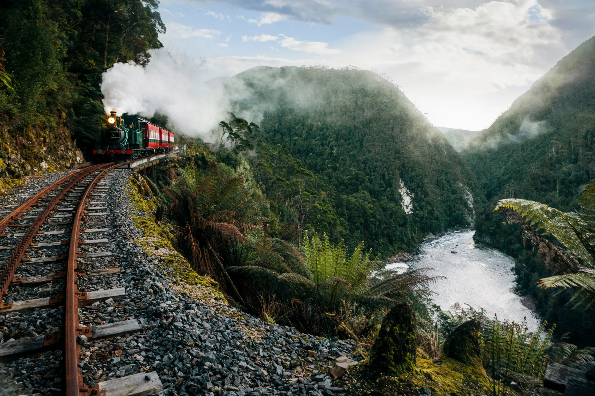 A West Coast Wilderness Railway steam train on the narrow mountain railway above a rainforest river gorge, Strahan