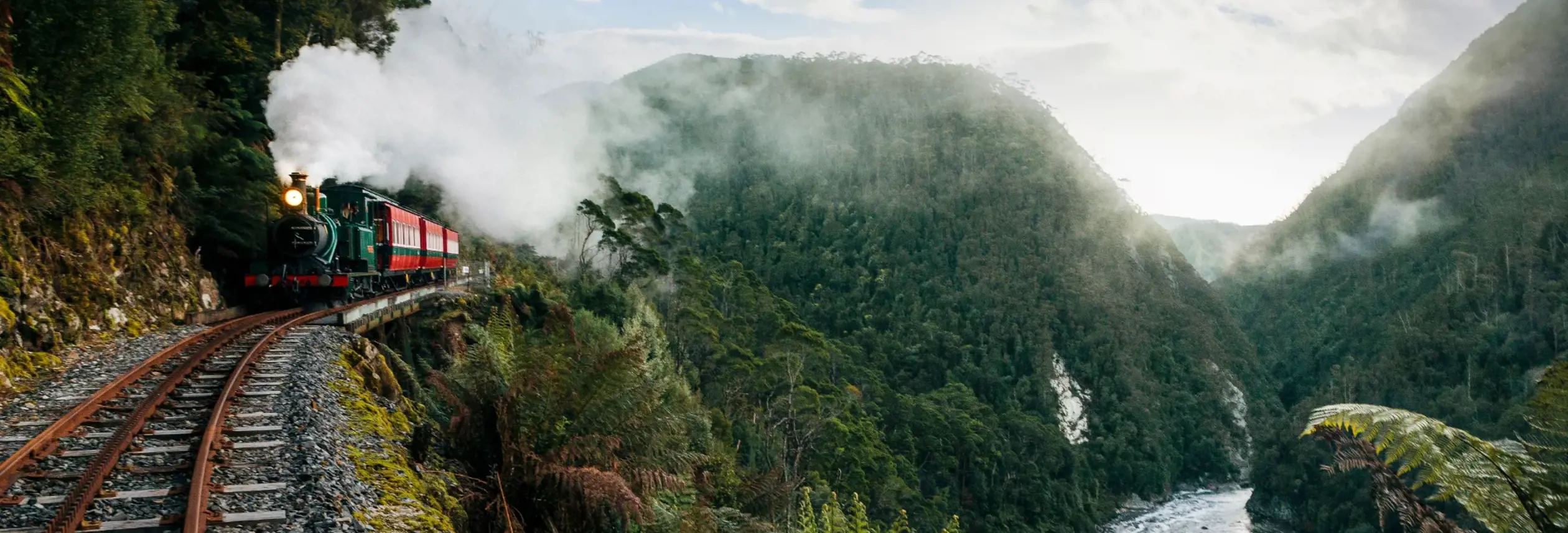 A West Coast Wilderness Railway steam train on the narrow mountain railway above a rainforest river gorge, Strahan
