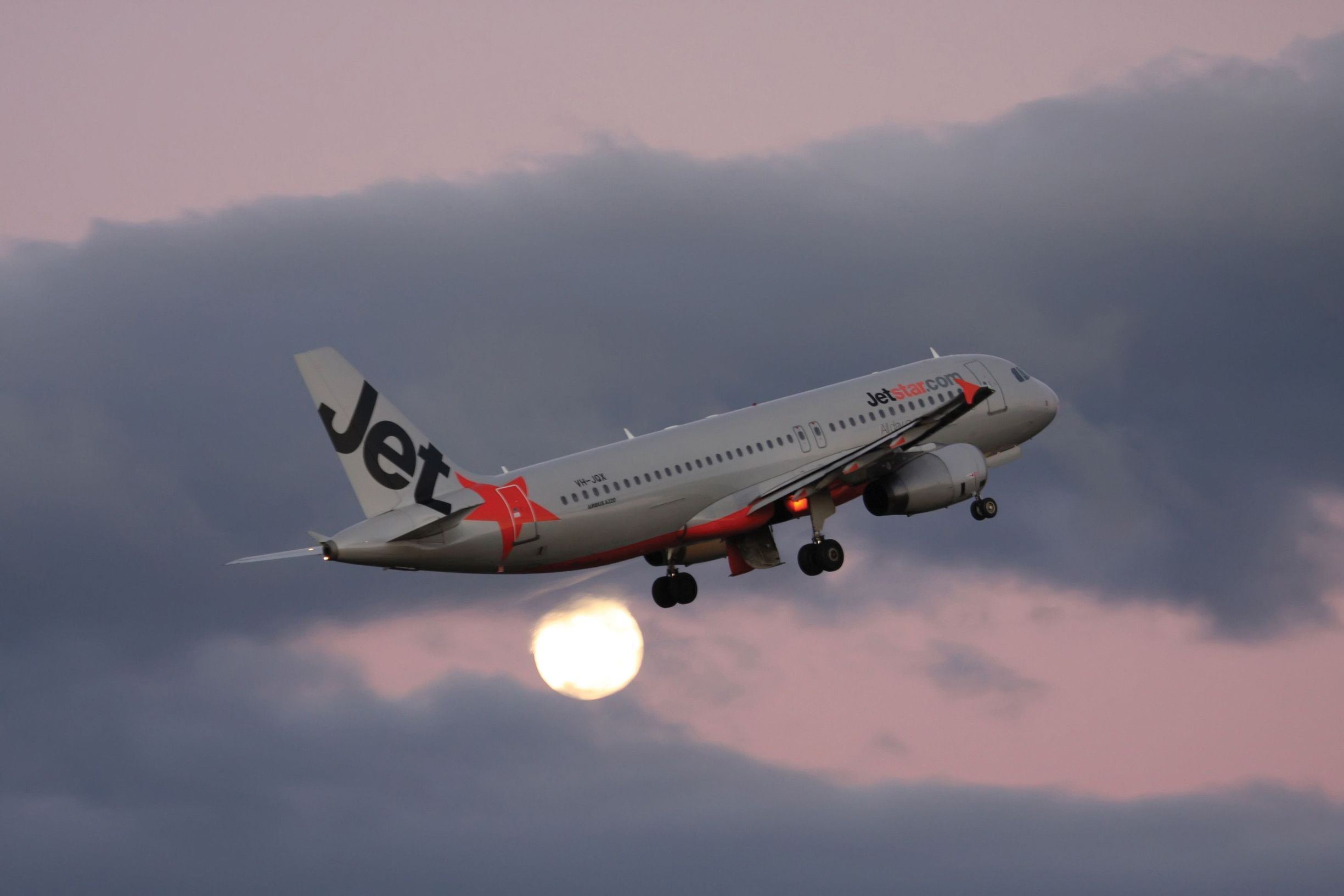 A Jetstar aircraft takes off against a pink dusk sky with the moon visible below at Launceston Airport