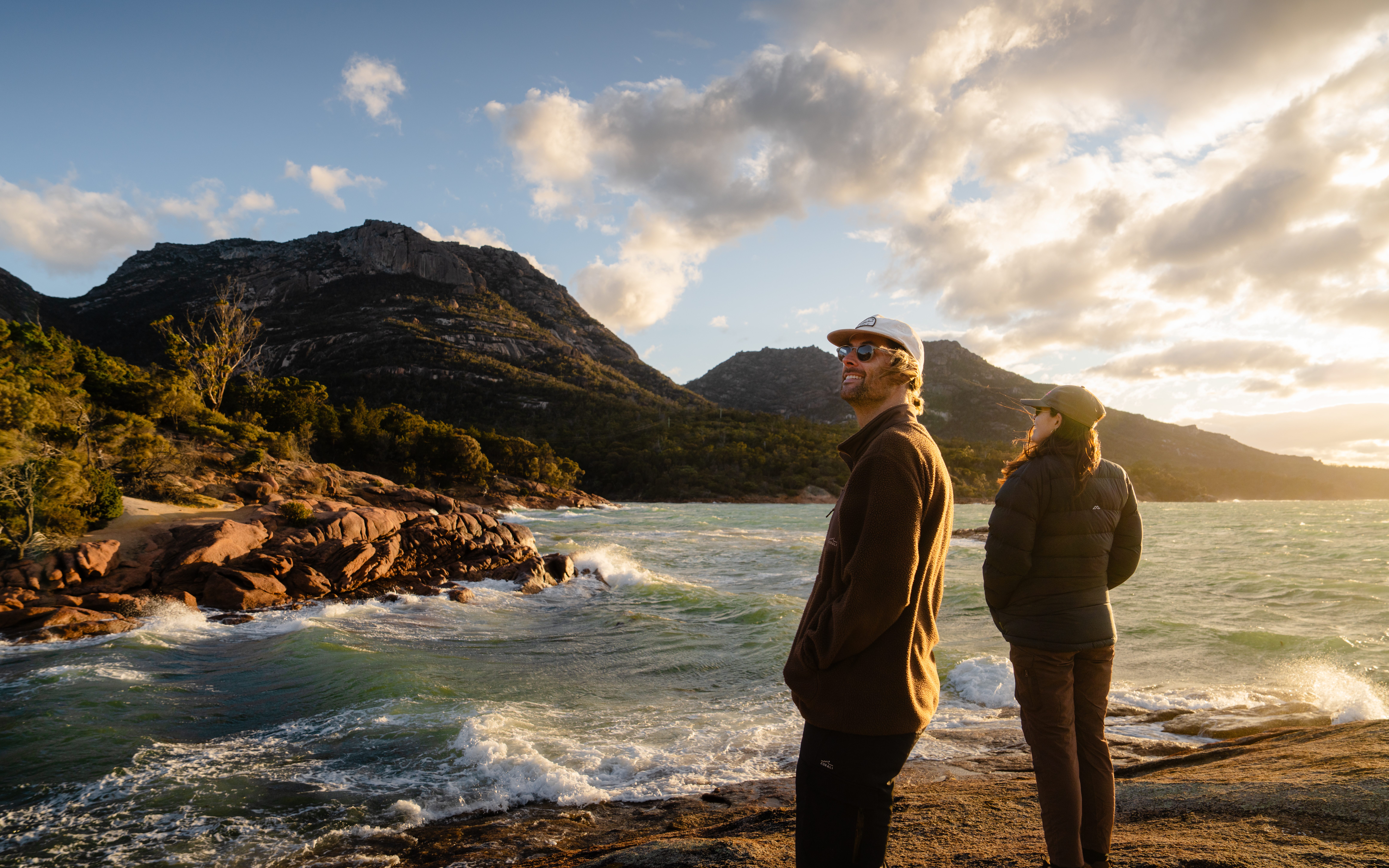 Two people on the rocky shoreline at Honeymoon Bay looking out over the bay, Freycinet National Park