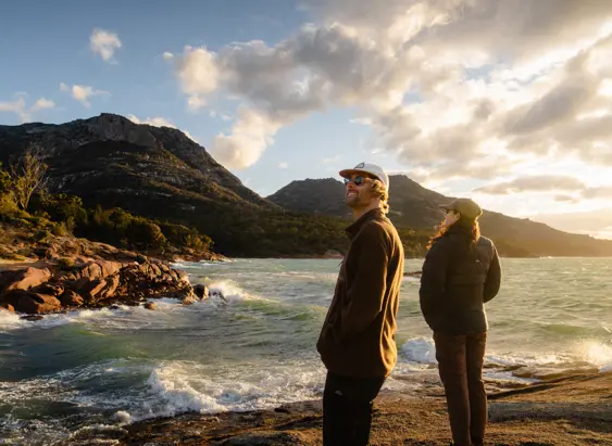 Two people on the rocky shoreline at Honeymoon Bay looking out over the bay, Freycinet National Park