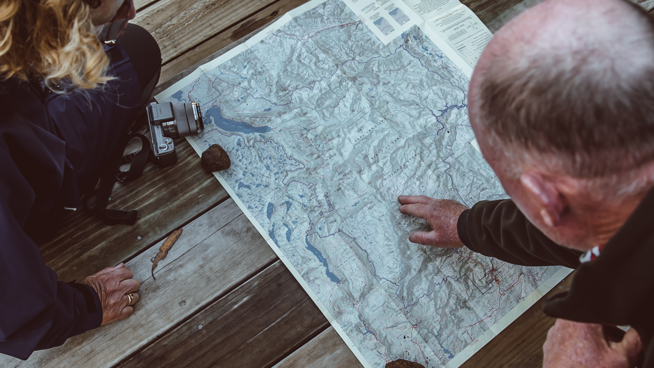Overhead view of two people studying a map of Cradle Mountain-Lake St Clair National Park, planning their Overland Track walk