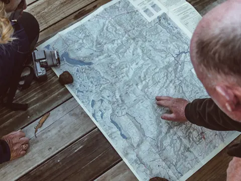 Overhead view of two people studying a map of Cradle Mountain-Lake St Clair National Park, planning their Overland Track walk