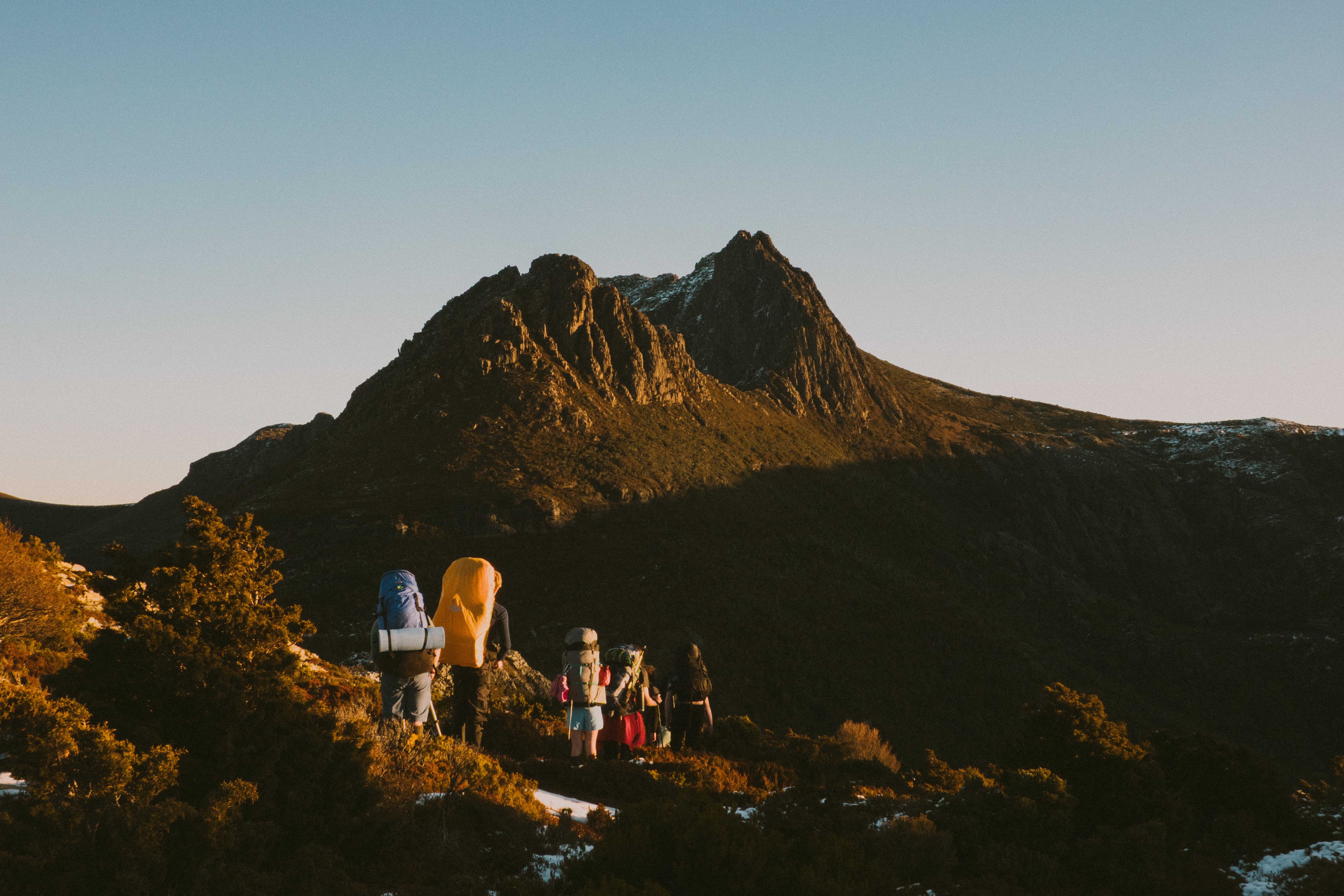 A group of hikers with large backpacks on the Cradle Summit Walk track with the twin peaks of Cradle Mountain ahead